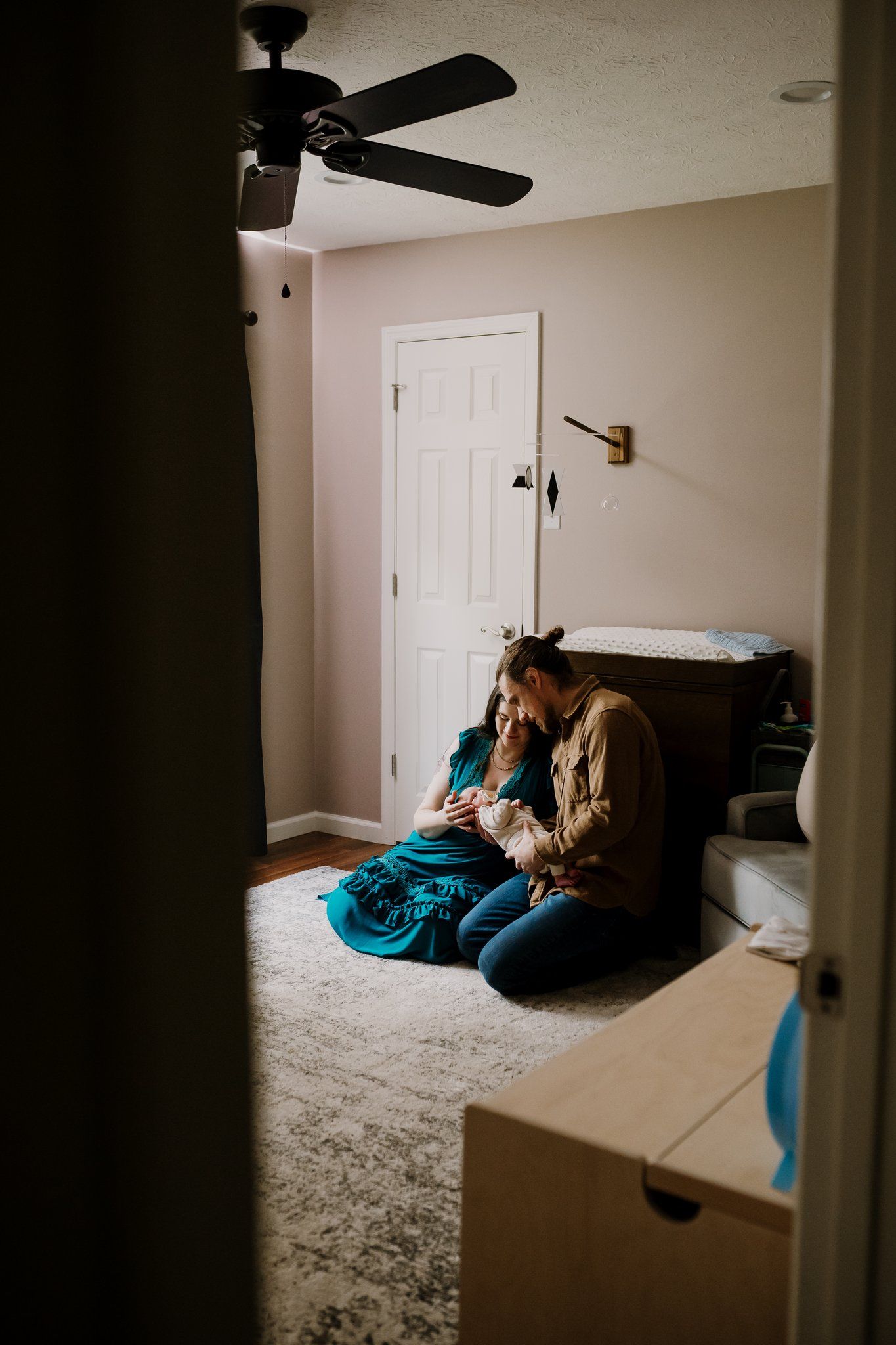 Parents sit on nursery floor holding their newborn baby