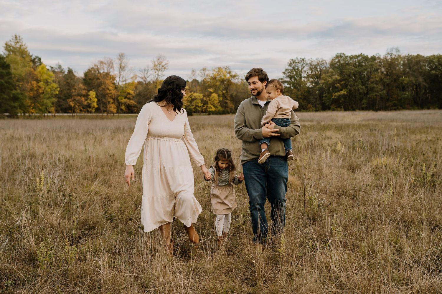 Family holding hands walks through a field during fall family photos