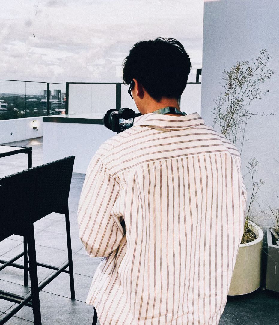 A photographer in a striped white shirt at a modern balcony workspace taking photos.