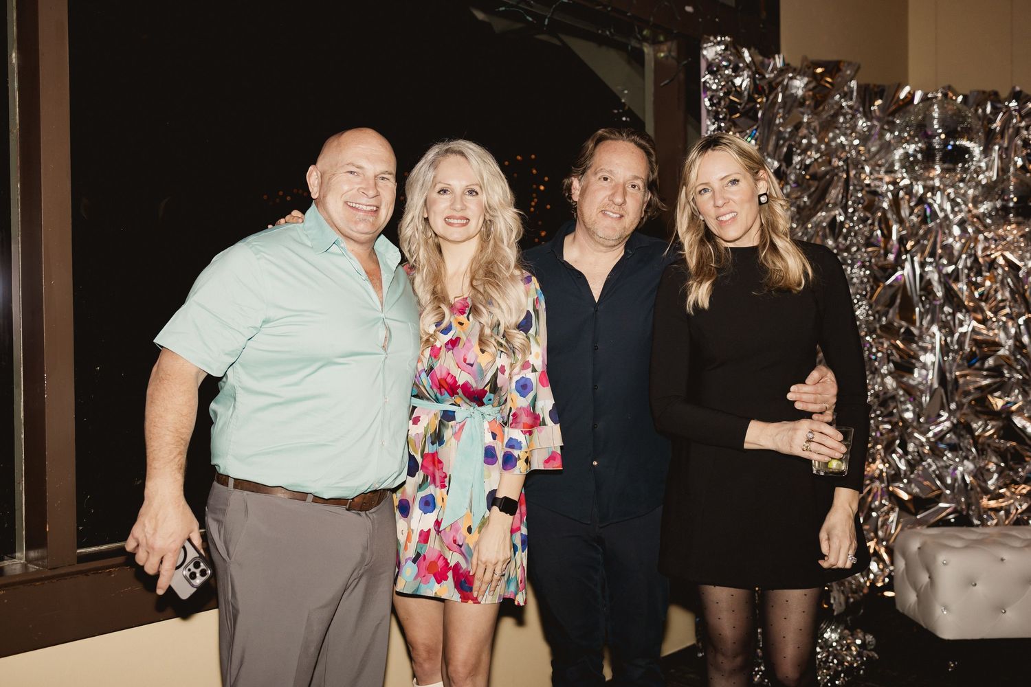 Two couples pose together at formal event with silver backdrop.