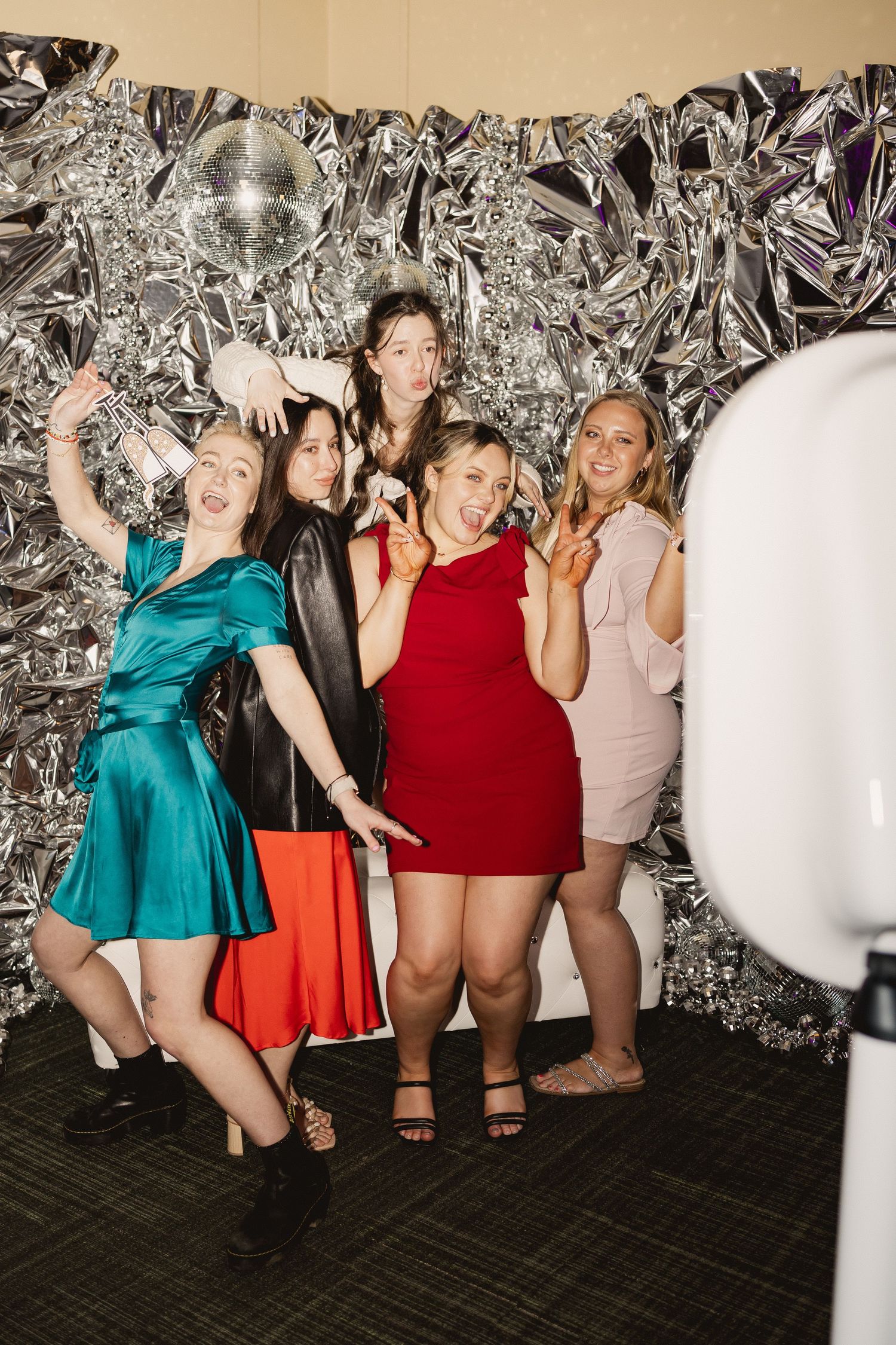 Group posing energetically in front of a silver foil backdrop at a party photo booth.