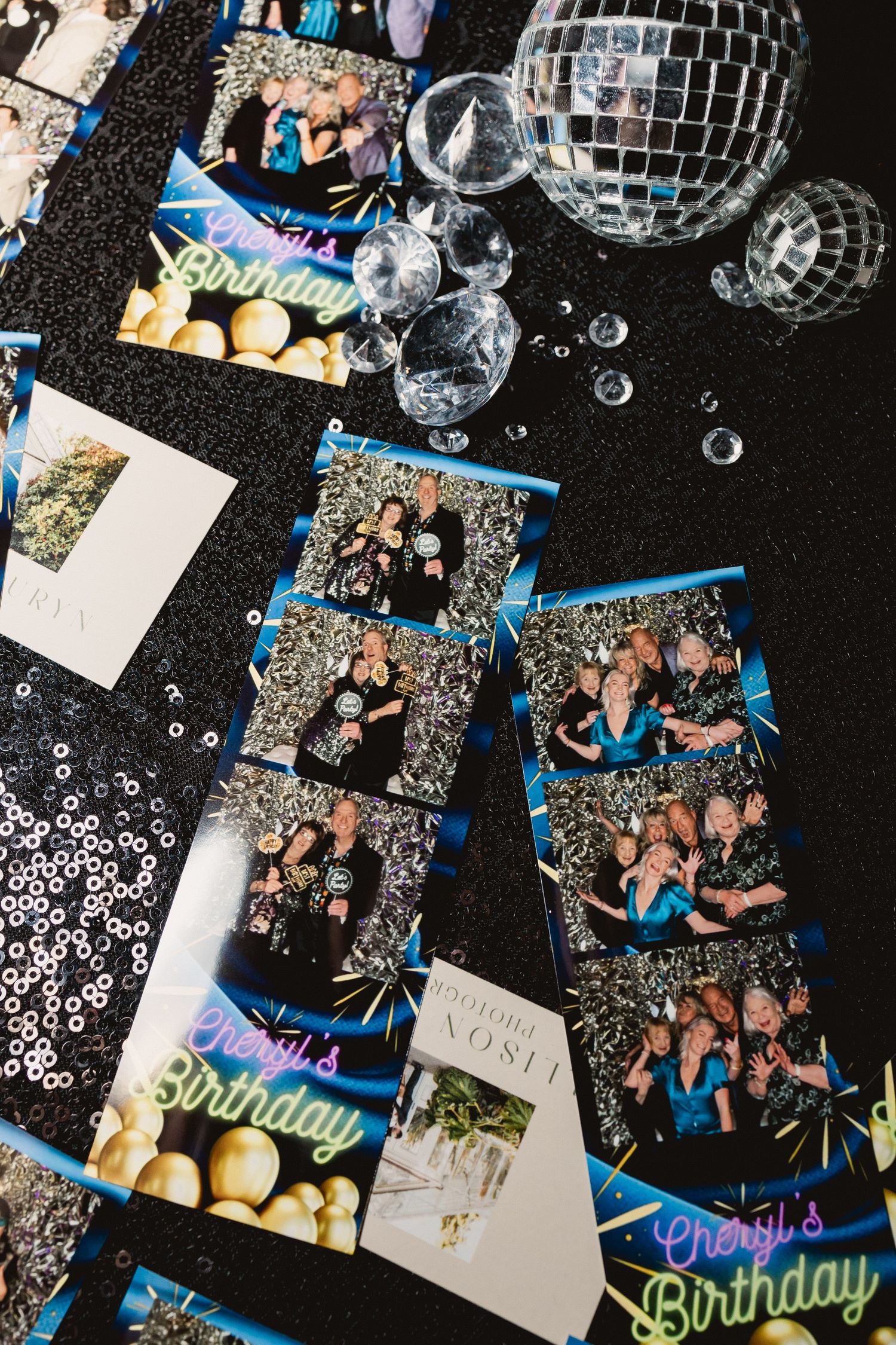 Photo booth prints and disco balls arranged on a black surface with scattered sequins and party decorations.