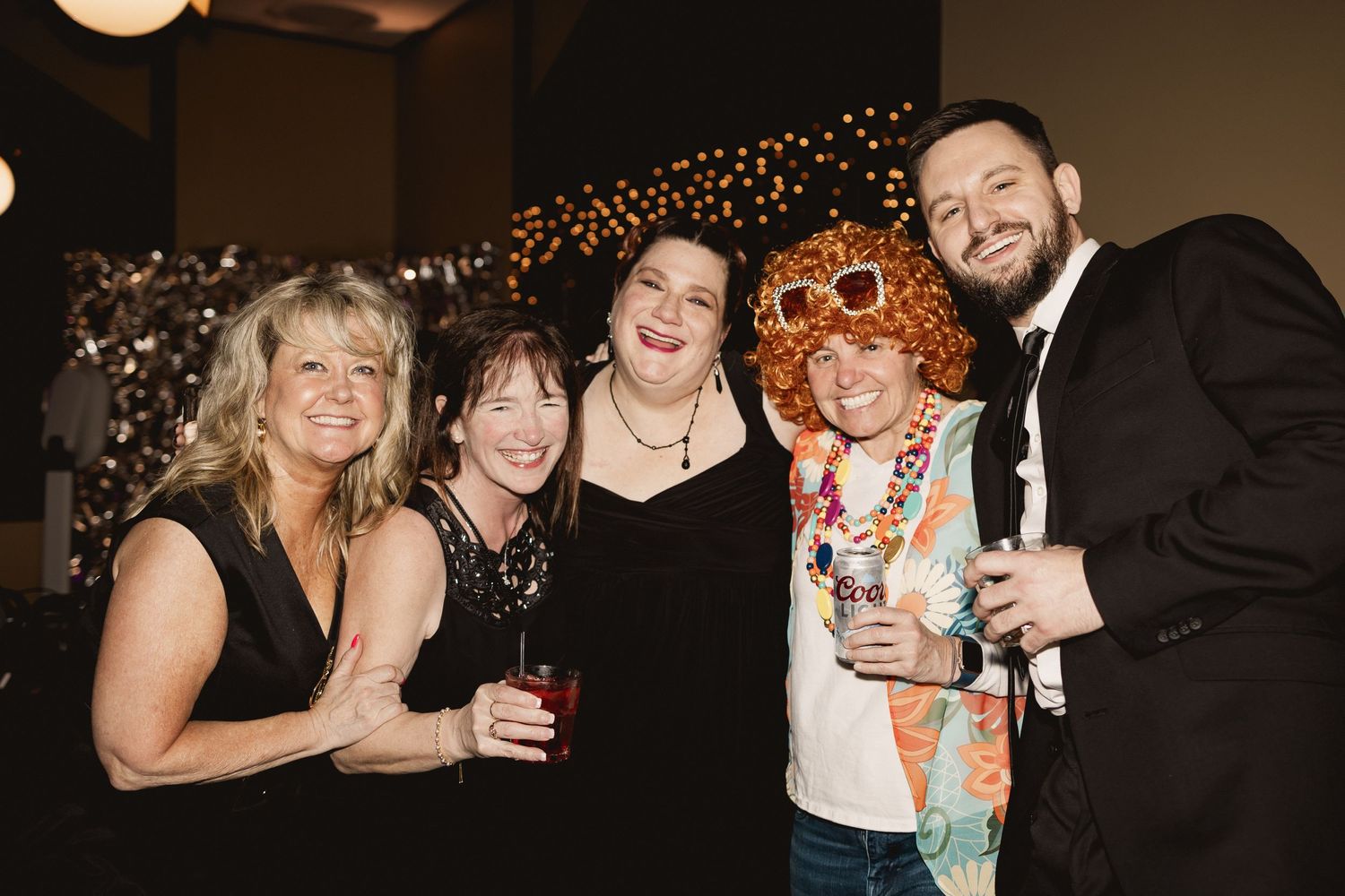A group in festive attire posing together at an evening celebration with sparkly decorations.