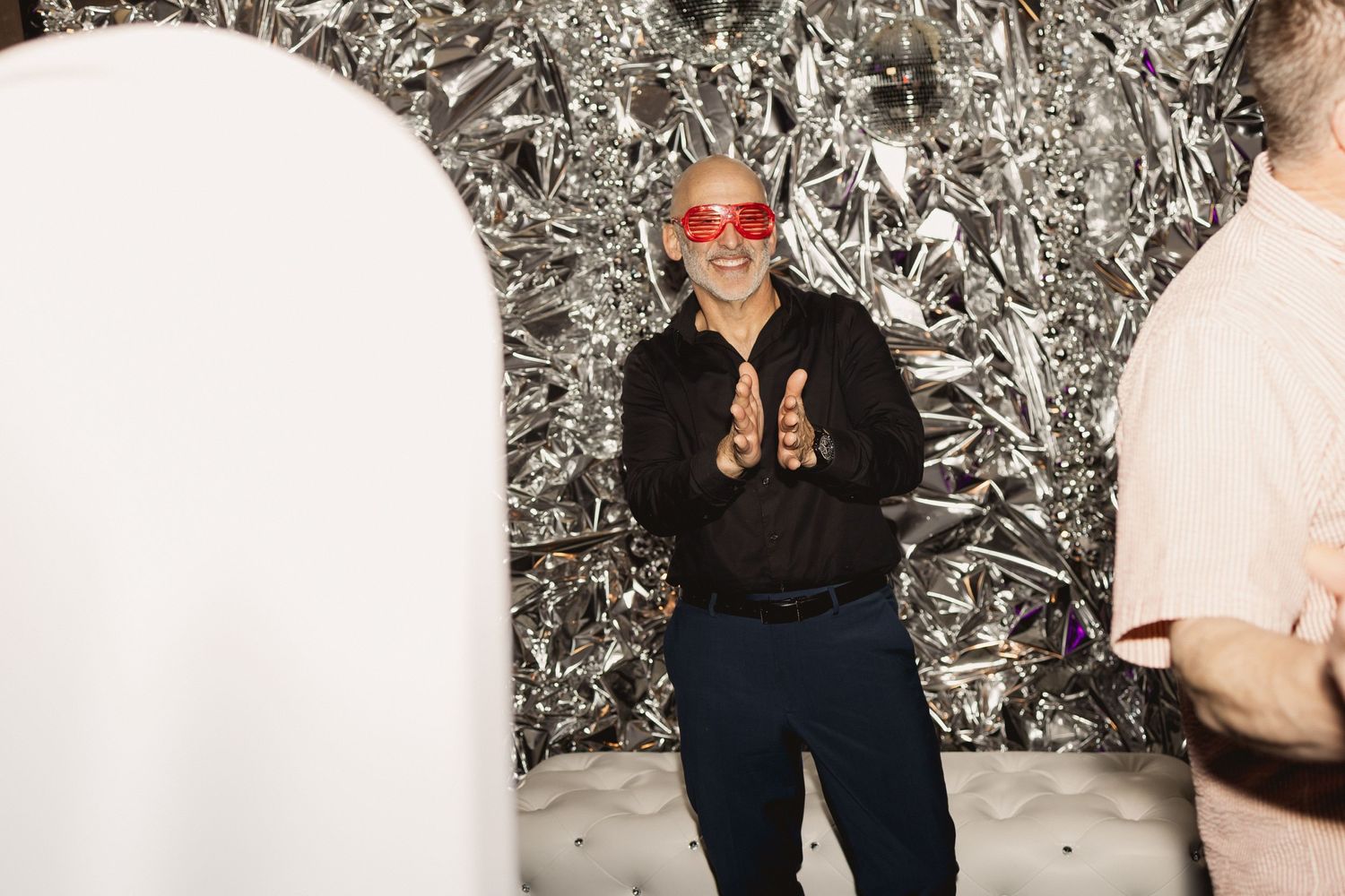 A party guest poses playfully in front of a silver tinsel backdrop at a photo booth.
