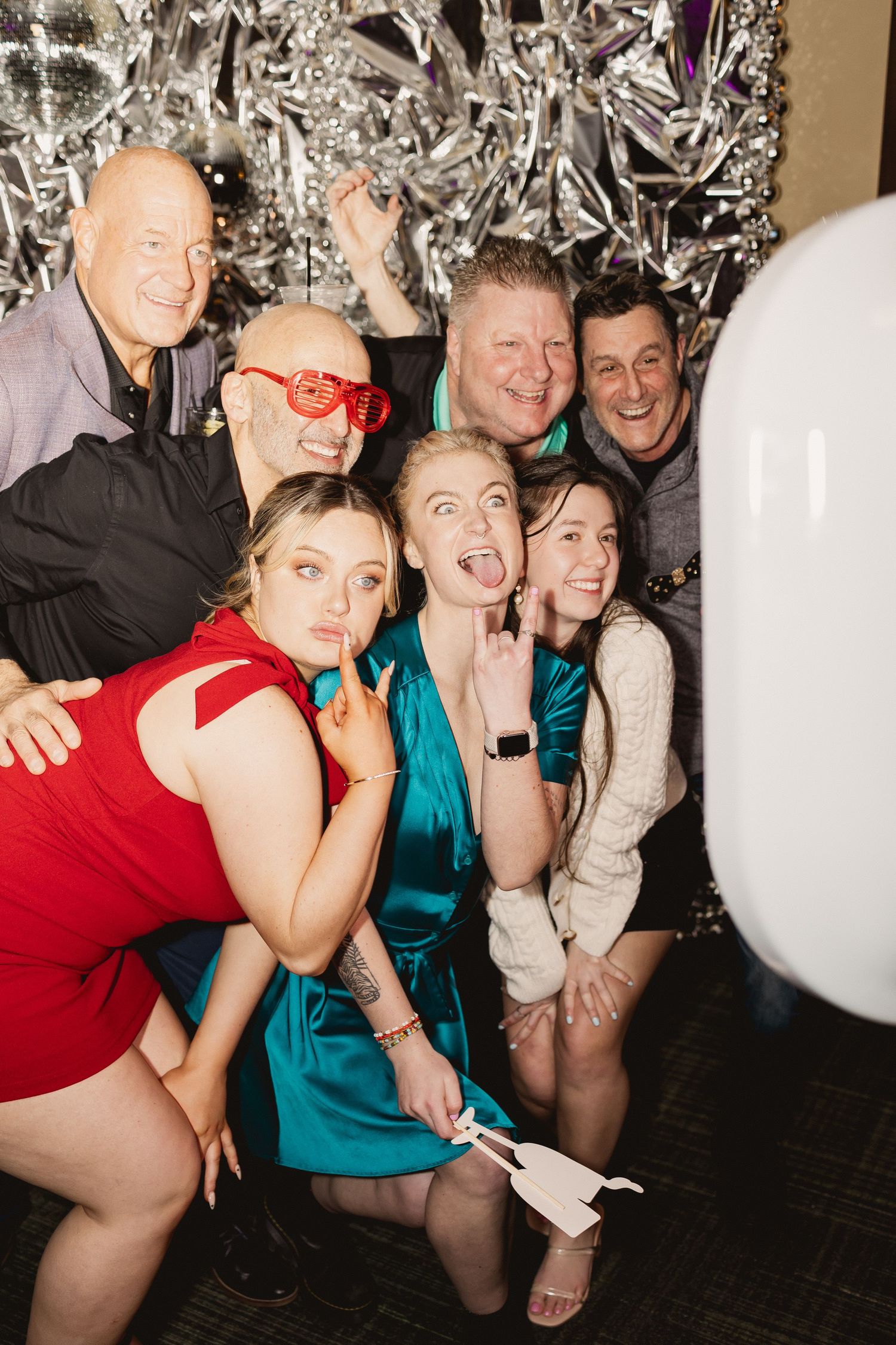 Friends making silly faces and poses in front of a metallic backdrop at a celebration.