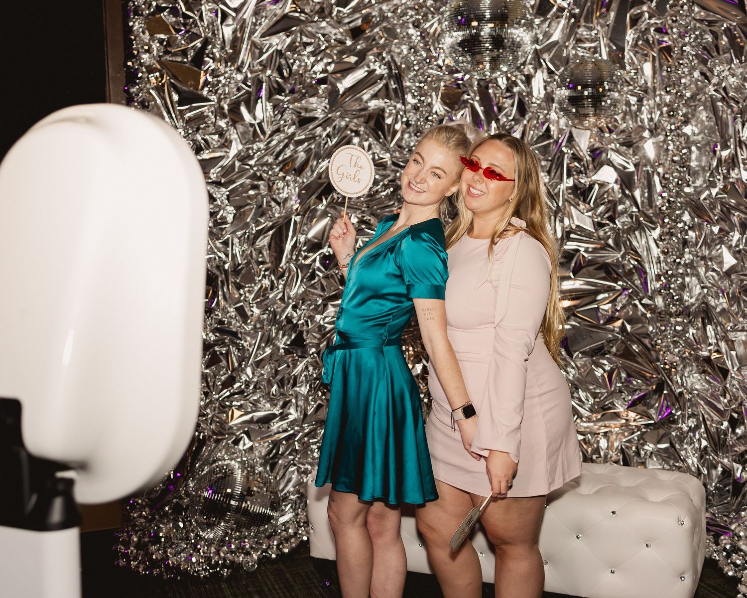 Two people posing in front of a silver metallic backdrop at a party photo booth.