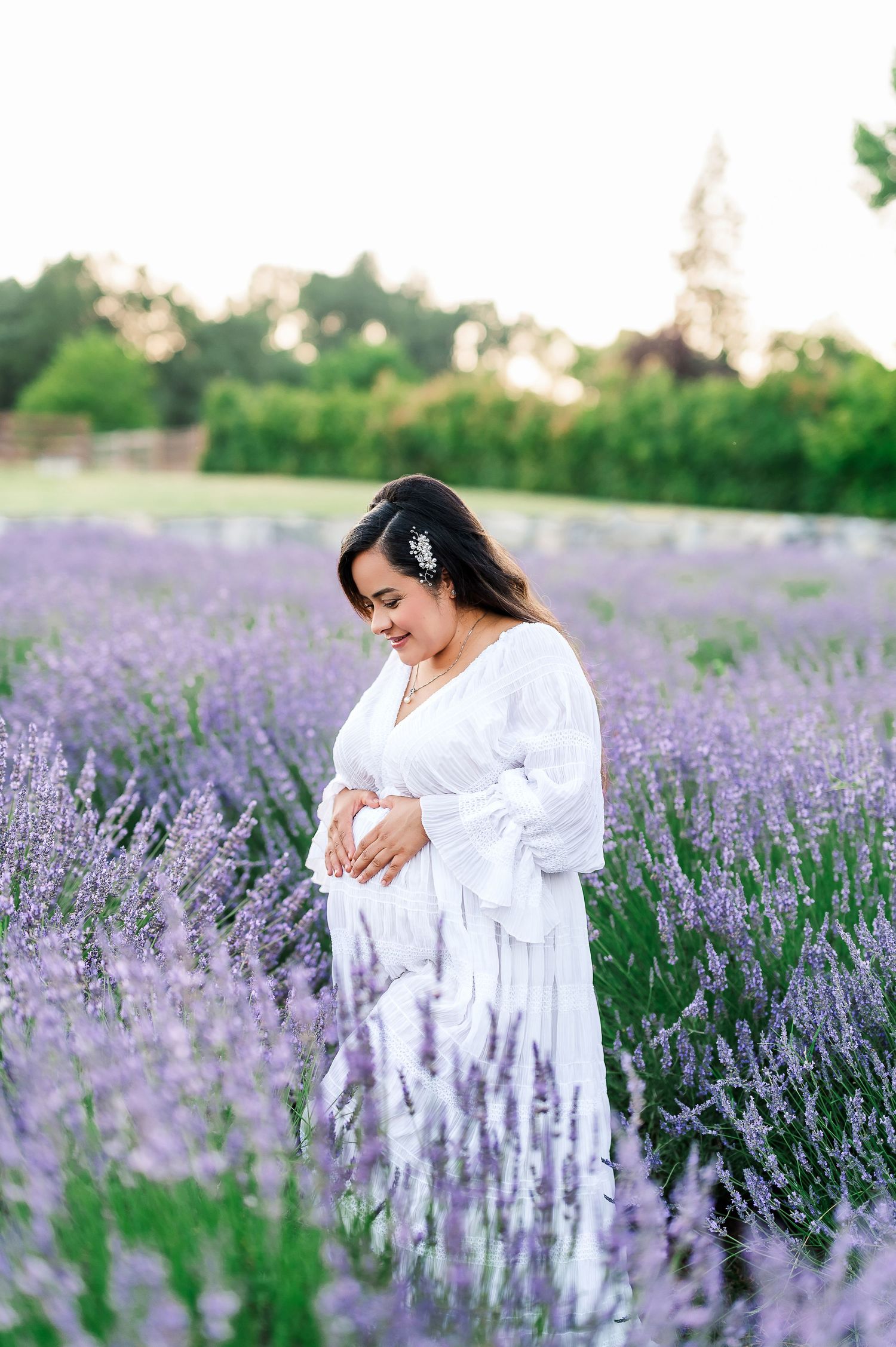 Woman in white dress standing in blooming lavender field at sunset.