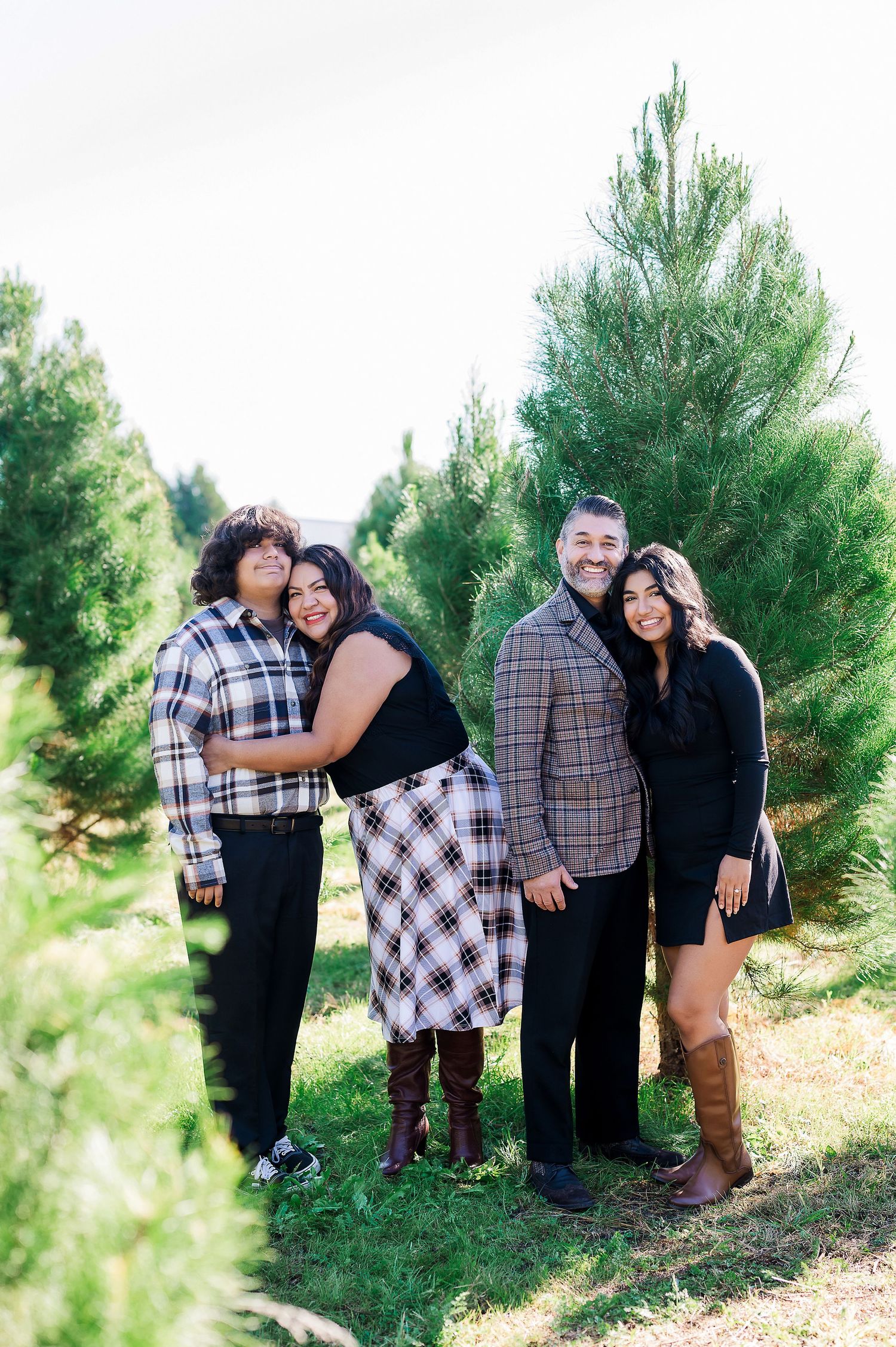 Two couples posing together in casual attire among tall pine trees.