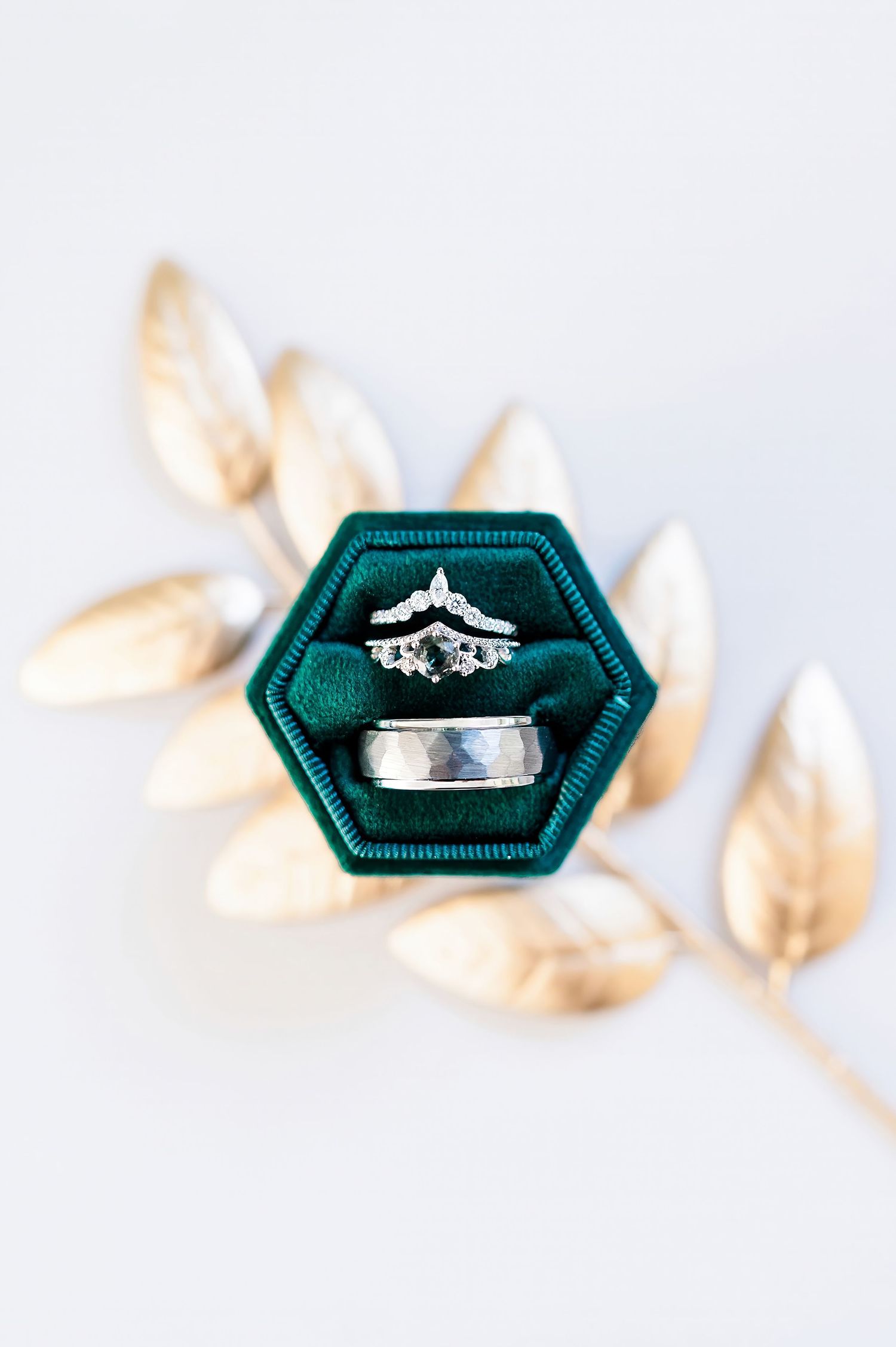 Wedding rings displayed in a dark green velvet hexagonal box with gold leaf accents.