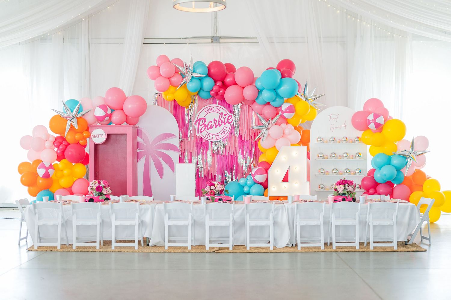 Colorful balloon garland and white chairs set up for children's birthday party in bright event space.