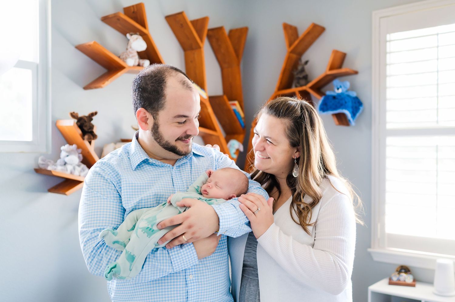 Young parents holding and admiring their newborn baby in nursery with wooden wall decor.