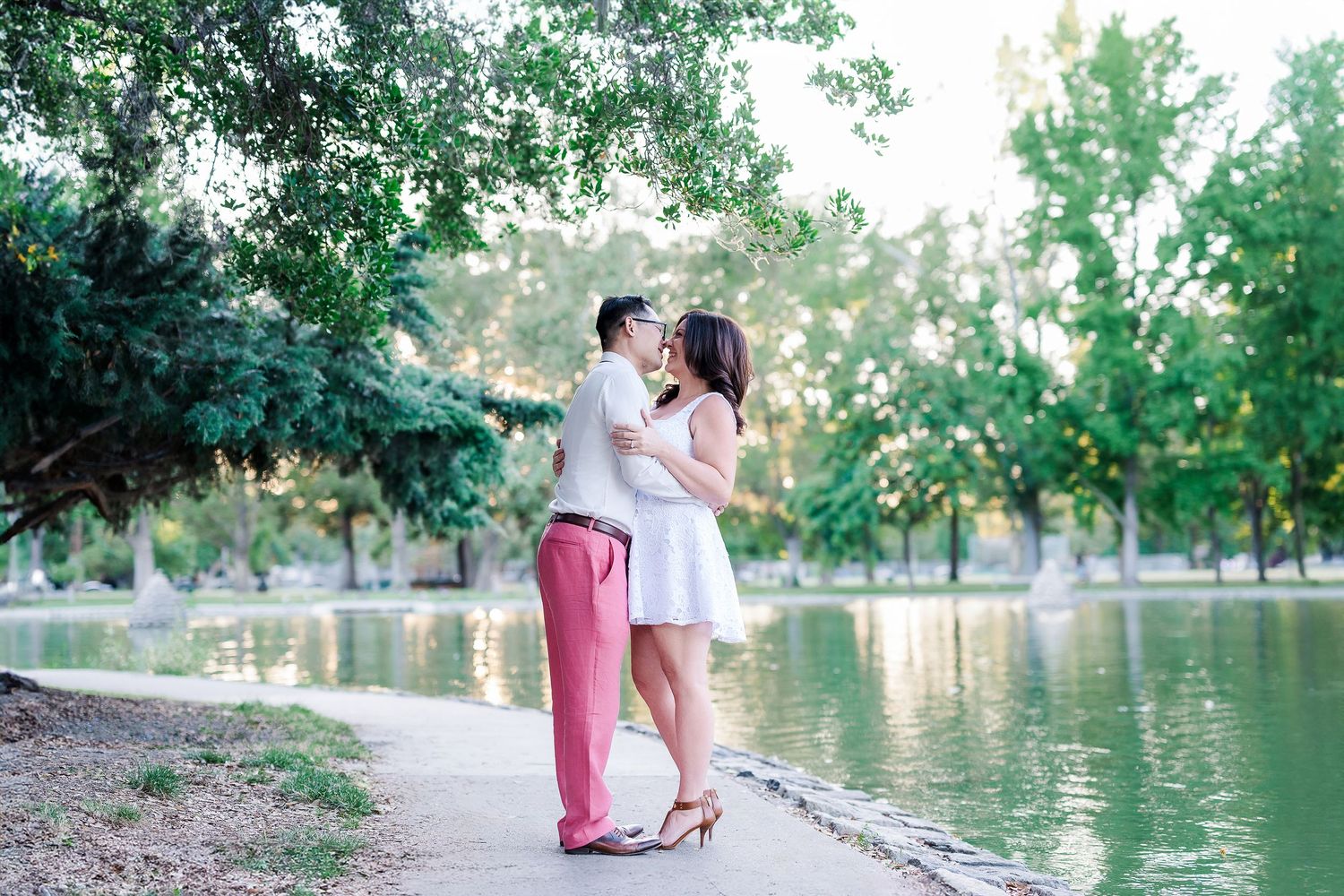 Romantic couple sharing an intimate moment by a lakeside path surrounded by trees.