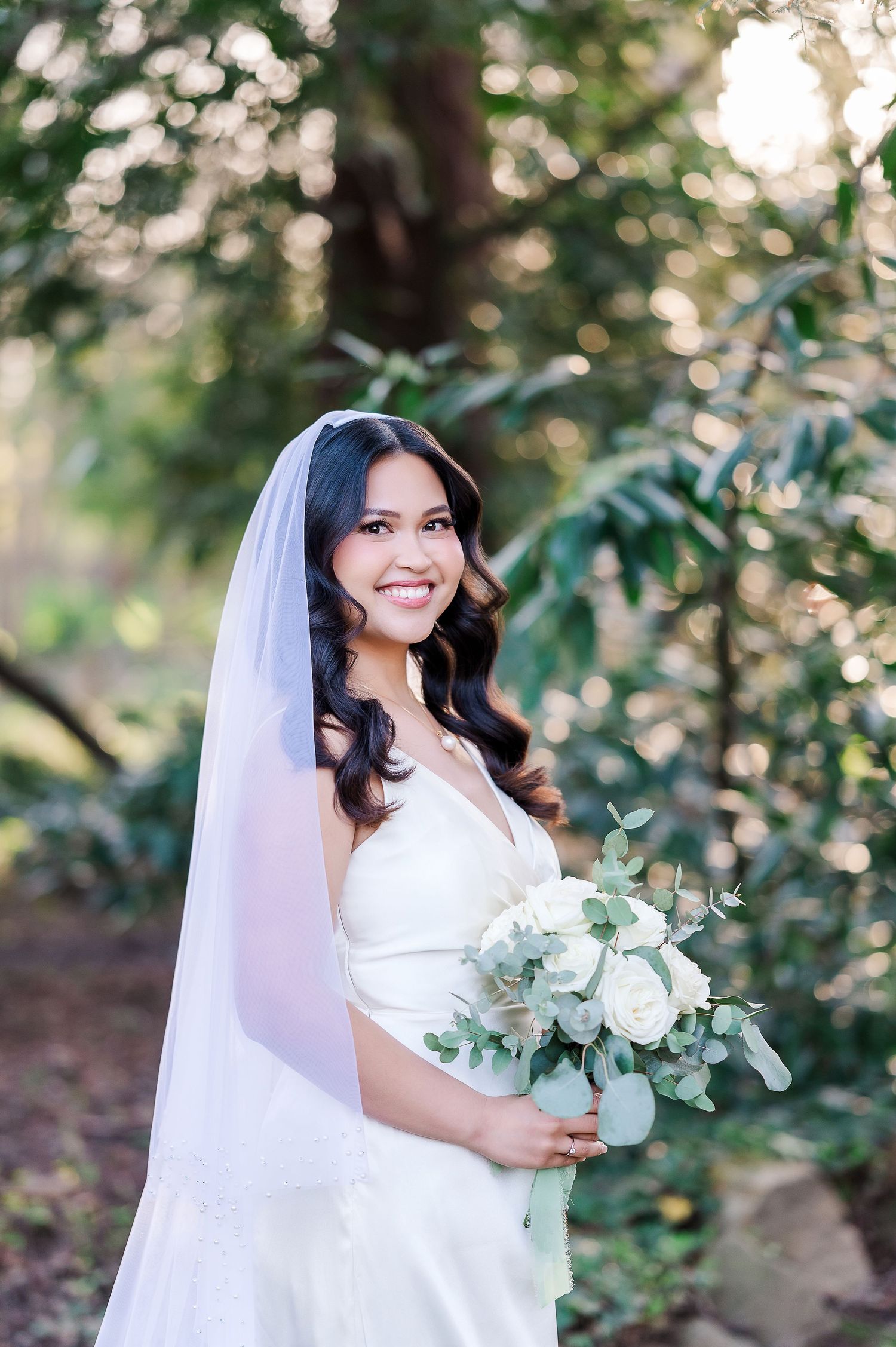 A bridal portrait in a natural garden setting with white bouquet and flowing veil.