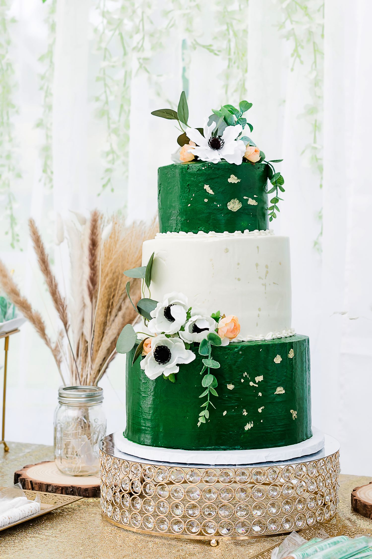Elegant three-tiered wedding cake with emerald green and white frosting decorated with anemone flowers and greenery.