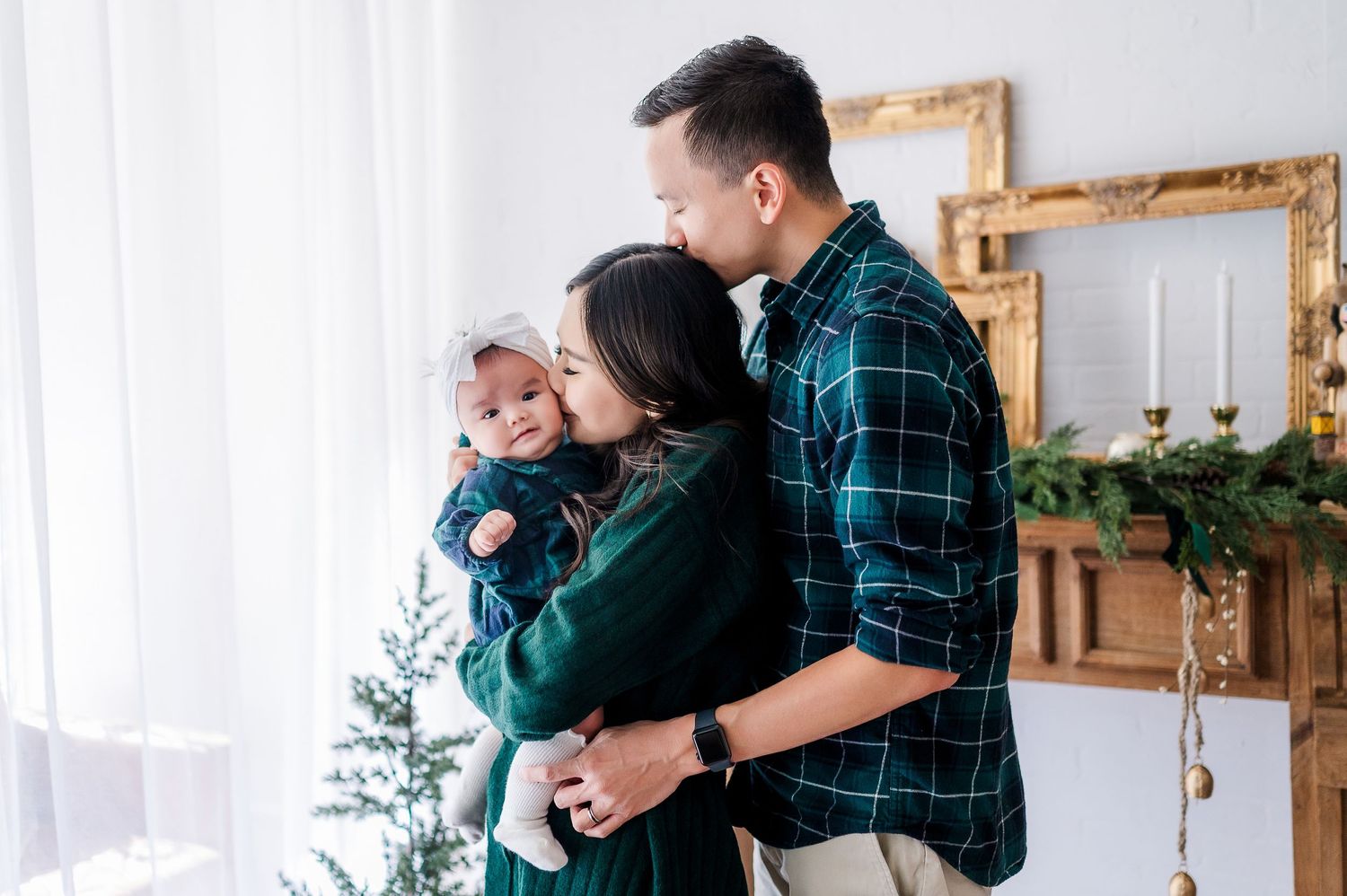 Family sharing tender moment with baby near decorated Christmas tree in bright room.