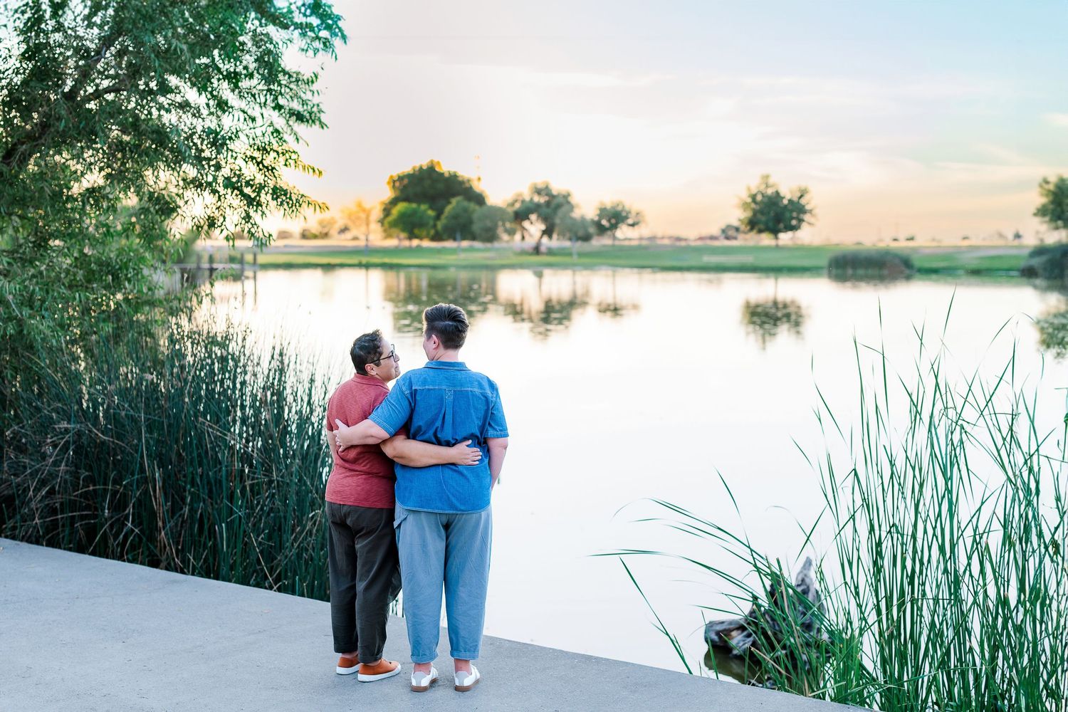 Couple standing together watching sunset by a serene lake with tall reeds.