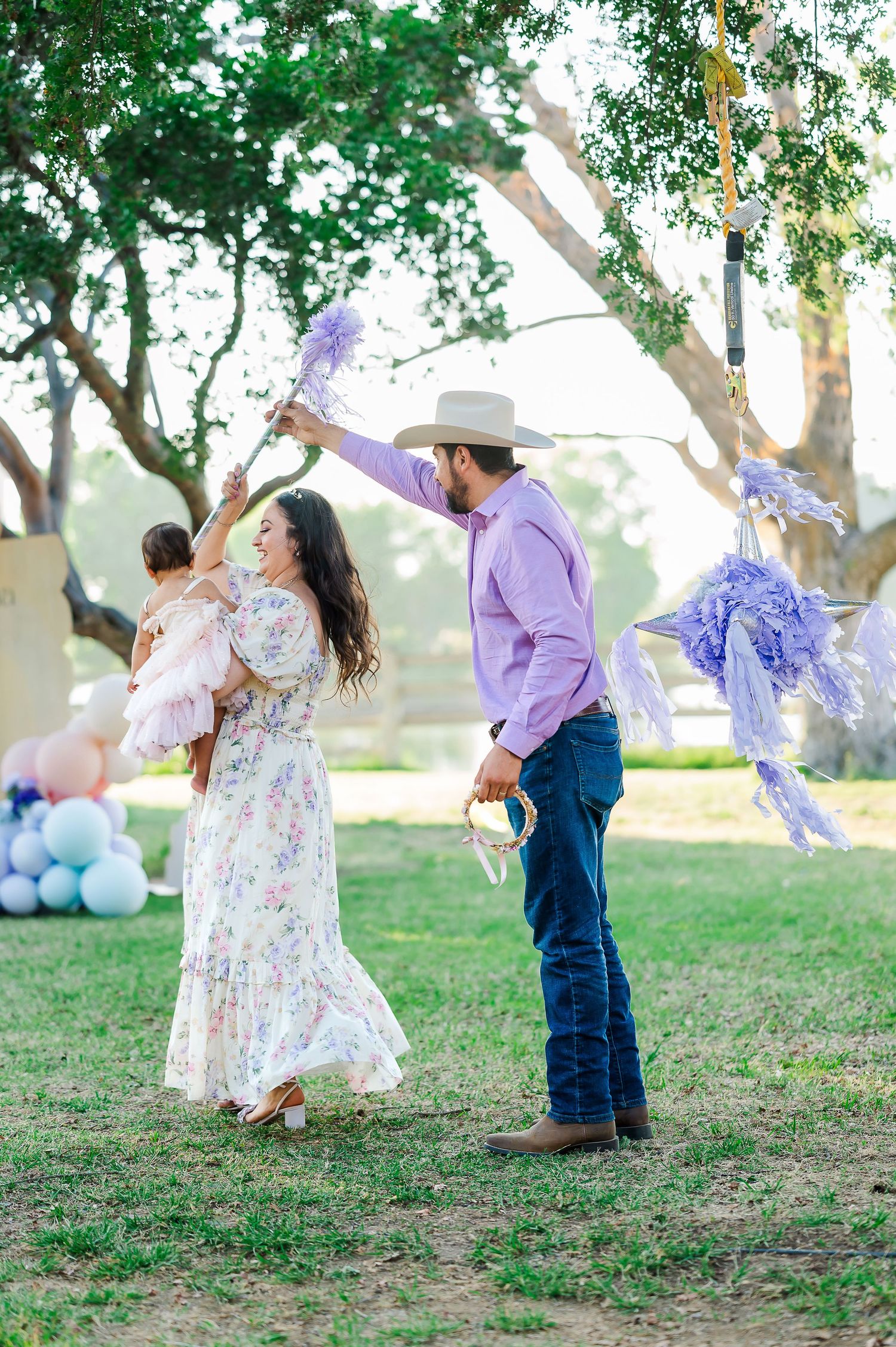 A candid outdoor family moment with purple decorations and balloons under green trees.