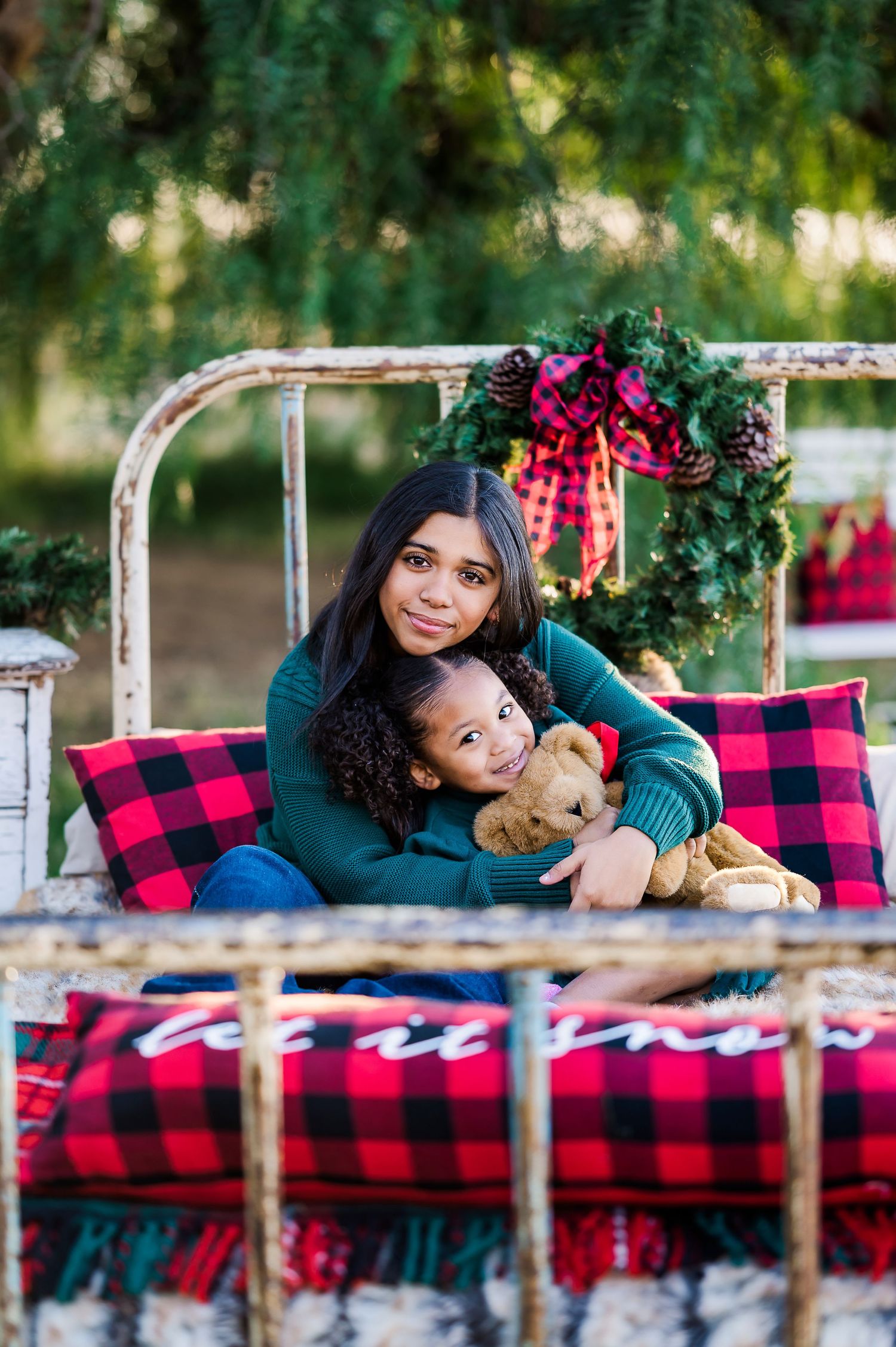 Mother and child lounging on vintage bed with buffalo plaid blankets and holiday decor.