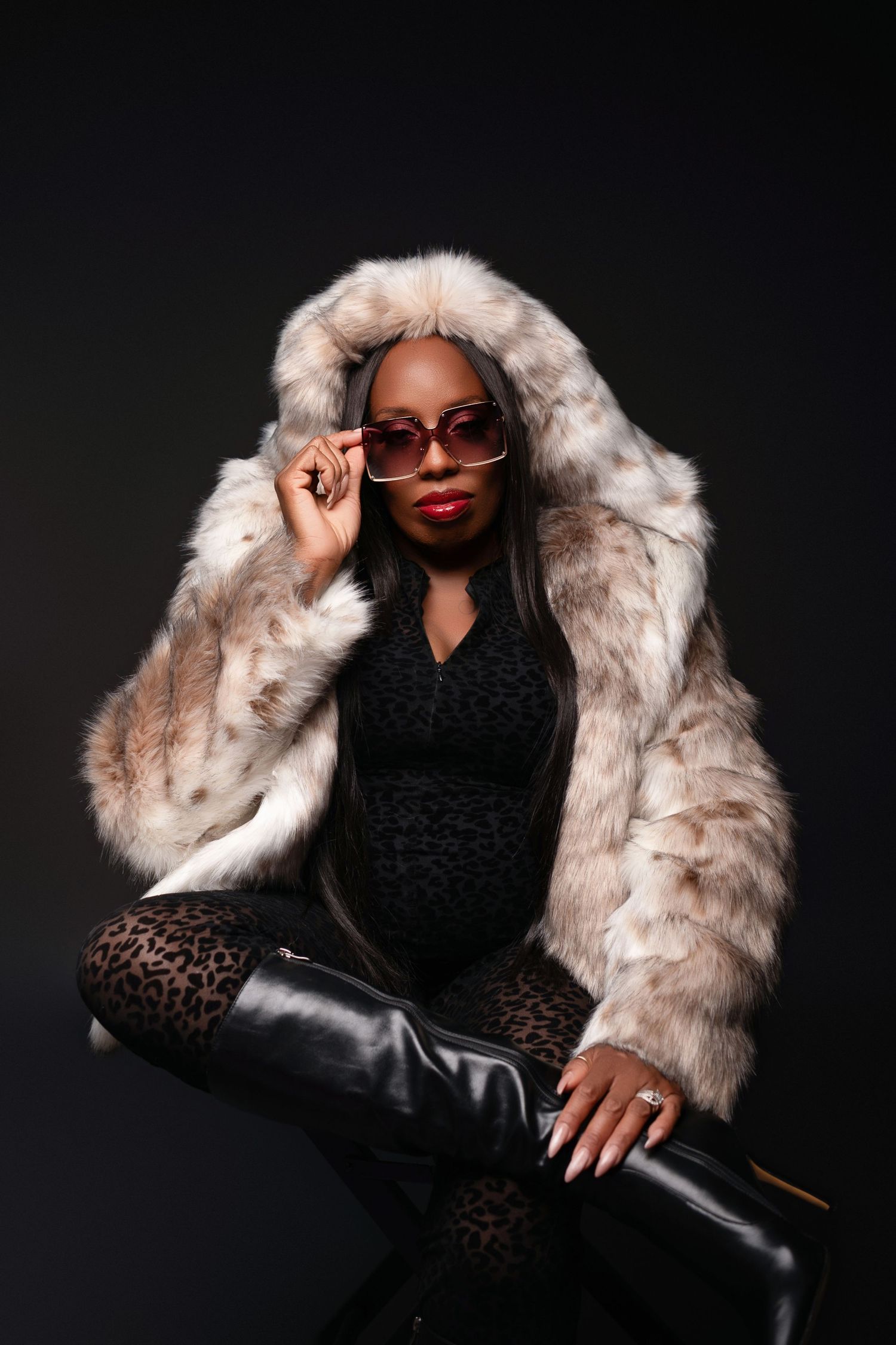 Glamorous portrait in faux fur coat and sunglasses against dark background.