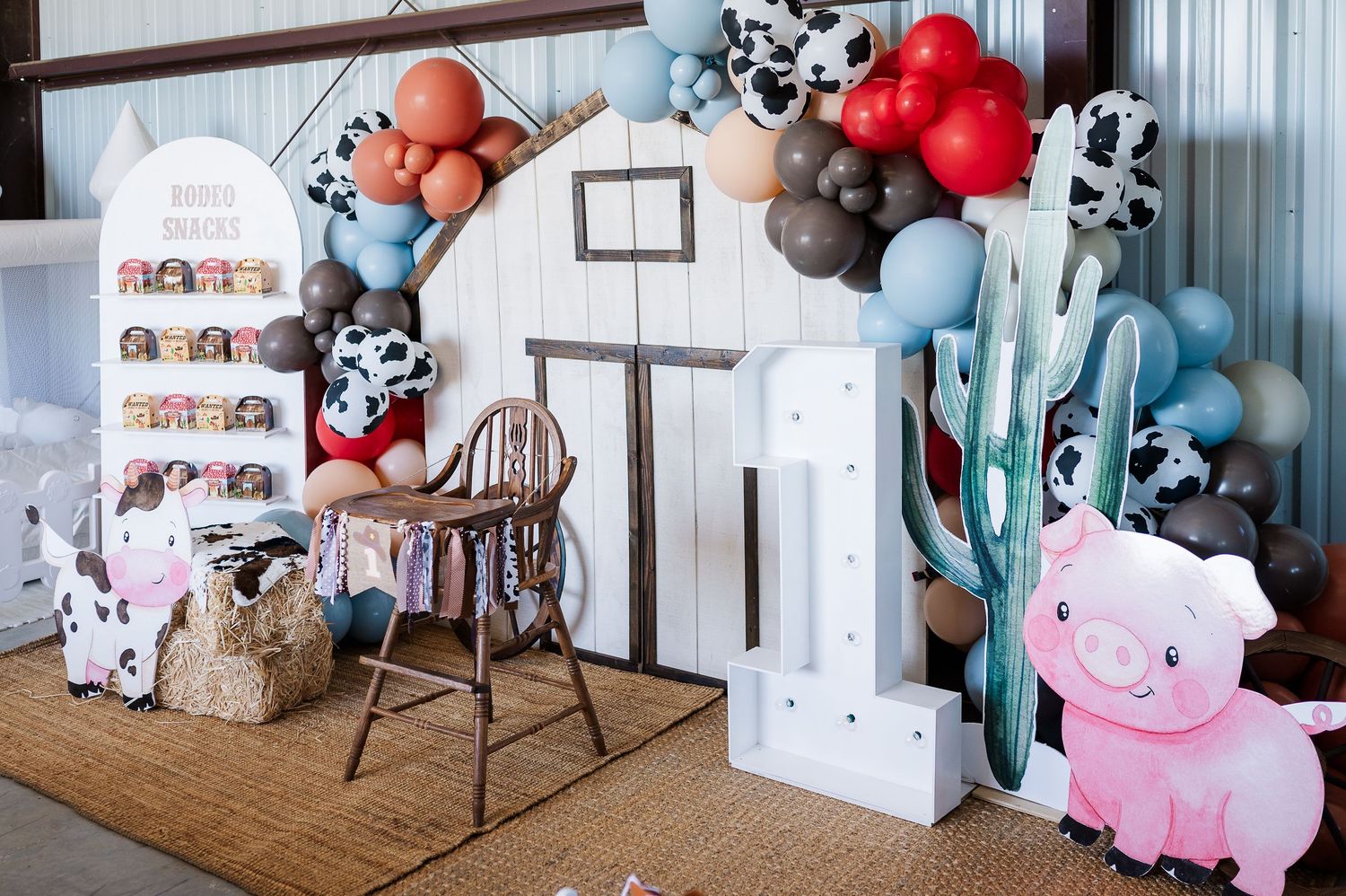 Western-themed party backdrop with balloon arch, cactus decor, and rustic wooden elements.