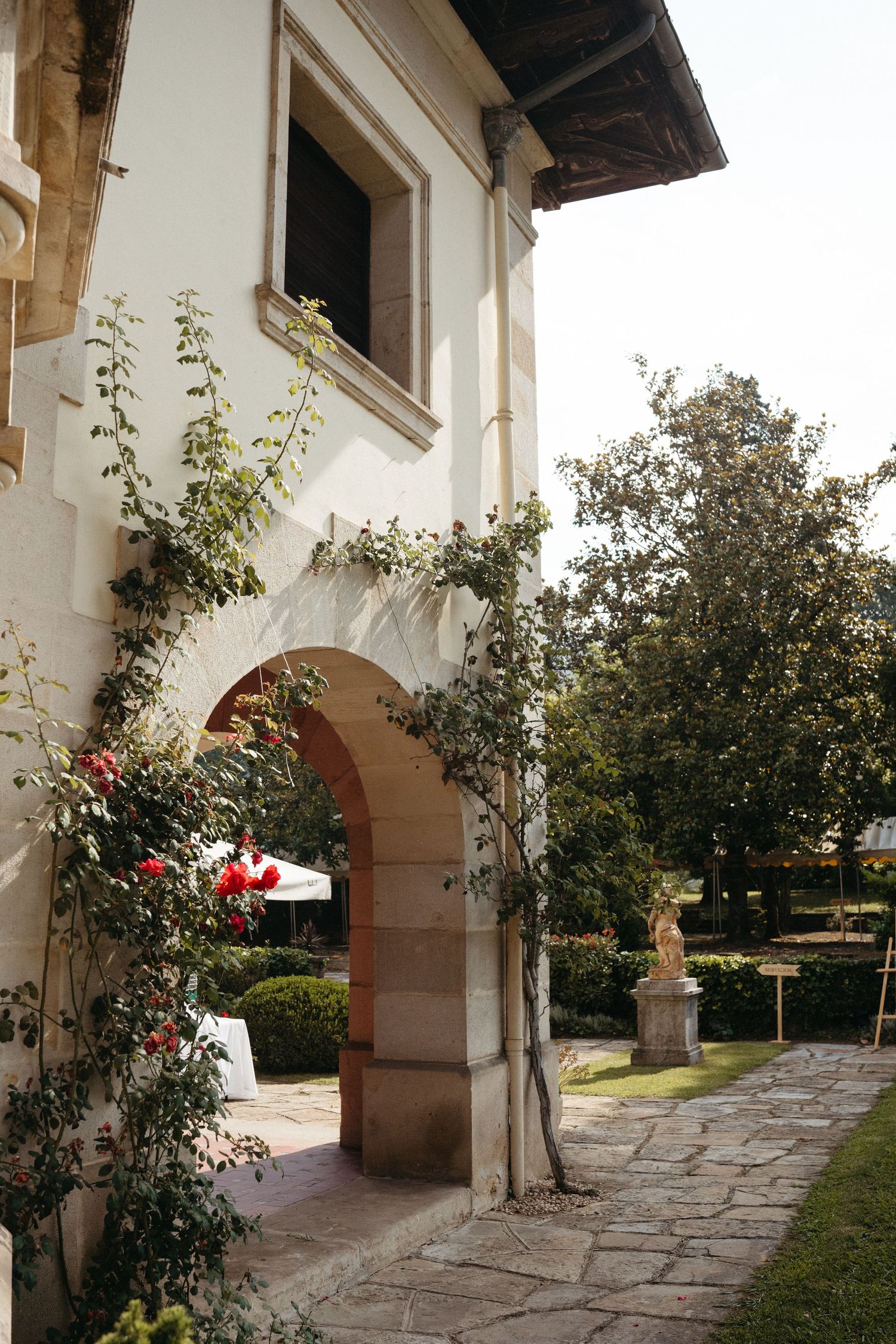 White stucco archway with climbing roses and a stone pathway leading to a garden.