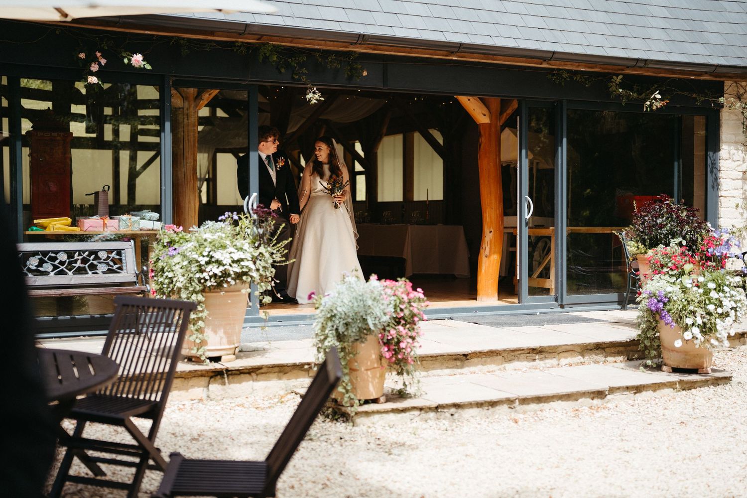 Rustic outdoor venue with timber beams and potted flowers decorating the entrance of a wedding reception space.
