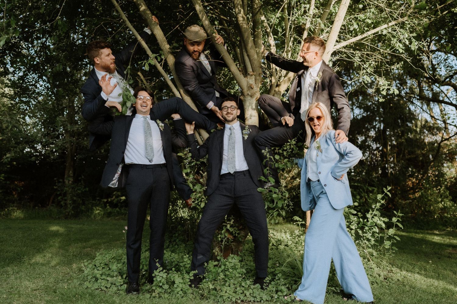 Wedding party celebrates joyfully on a sunny day in a garden setting.