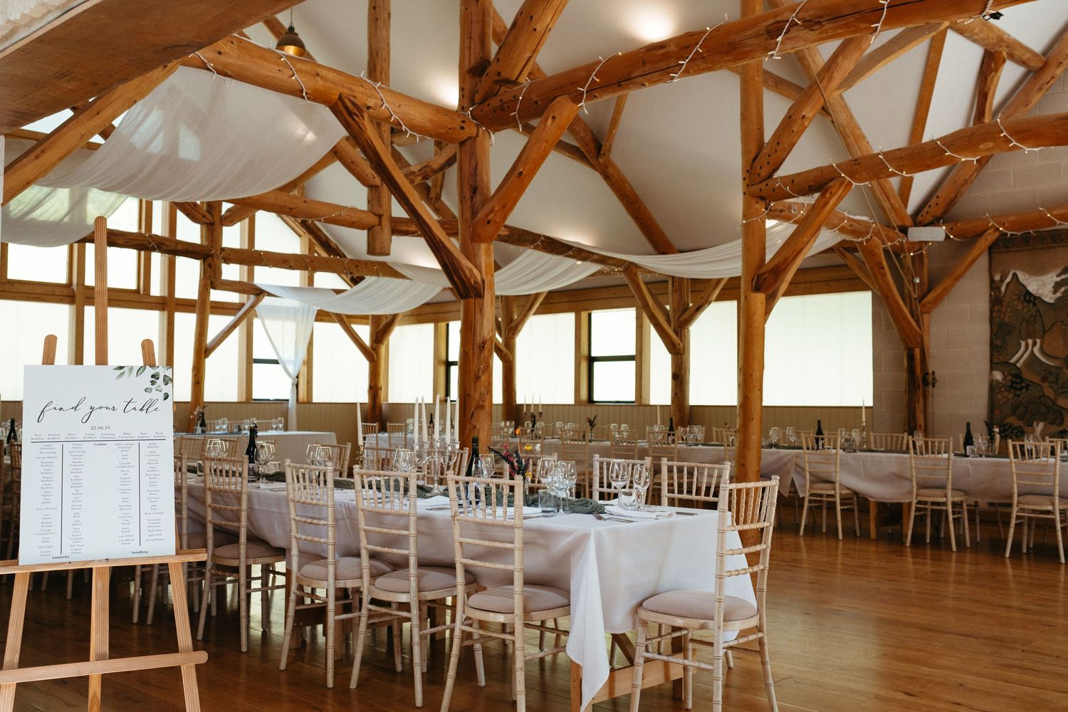 Elegant barn reception hall with exposed wooden beams and white tables set for a wedding celebration.