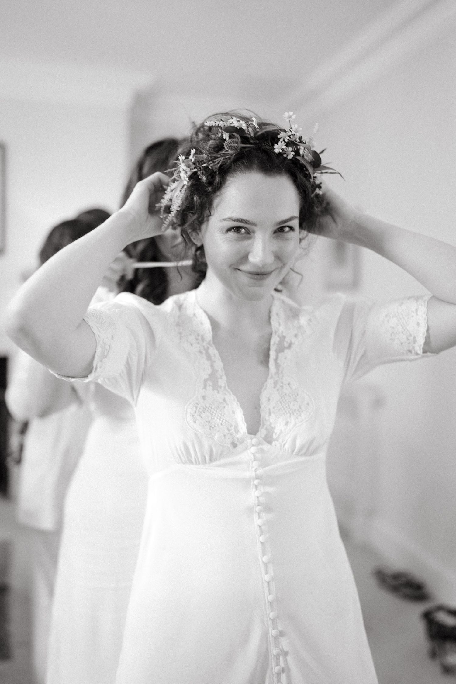 Black and white photograph of a bride in a vintage-style lace wedding dress with delicate buttons and floral crown.