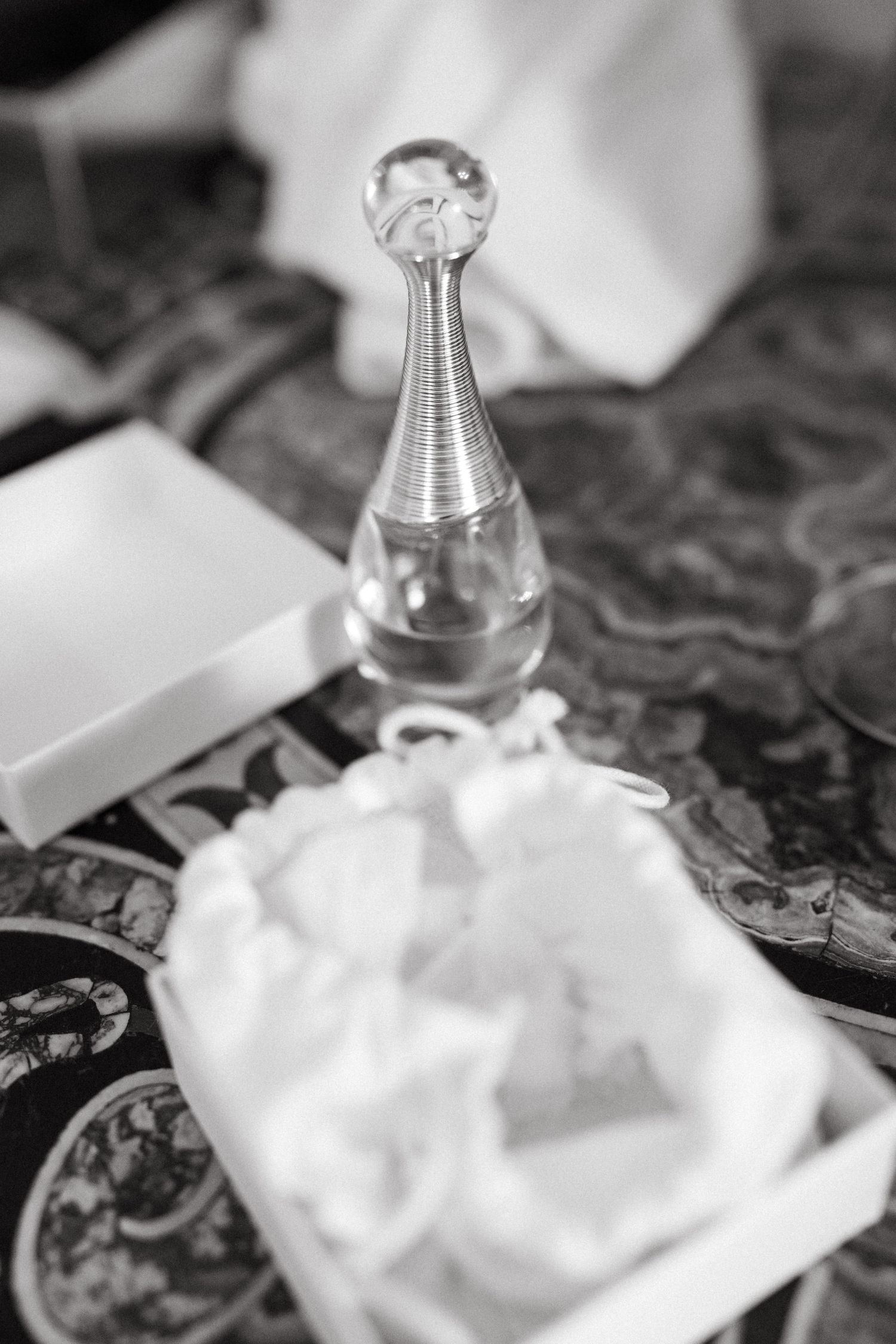 Elegant crystal perfume bottle on a patterned fabric with white details in black and white photography.