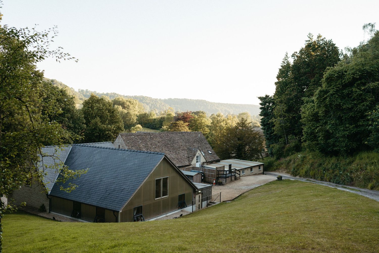 Modern country houses with slate roofs nestled in rolling green hills during golden hour.