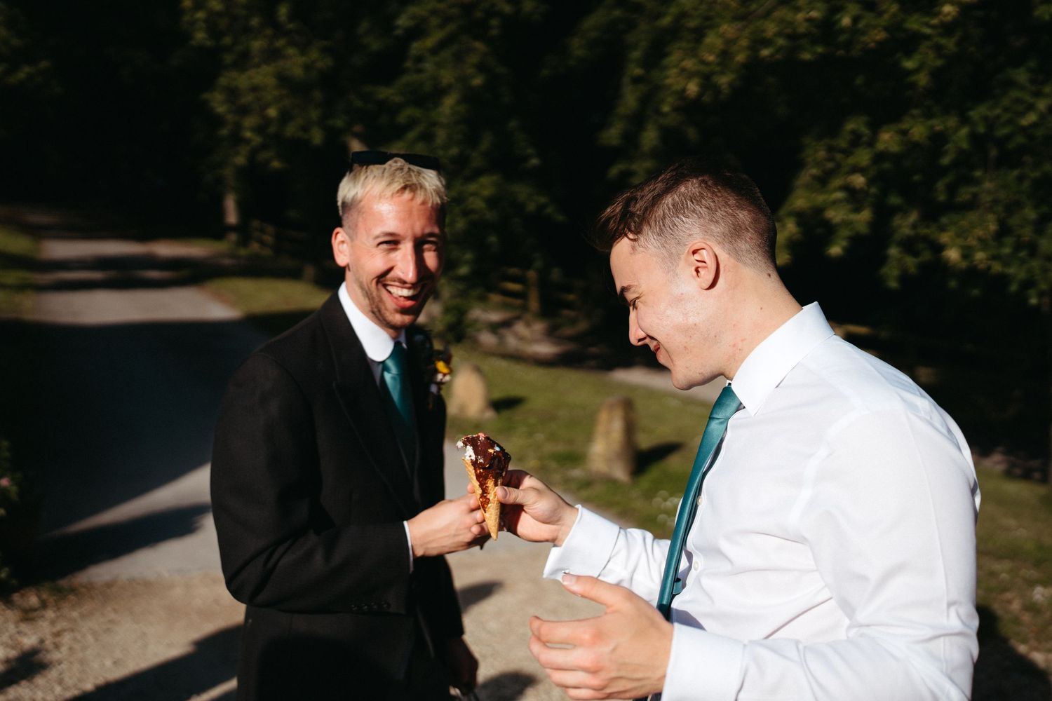 Two men laughing and sharing drinks outdoors on a sunny day.
