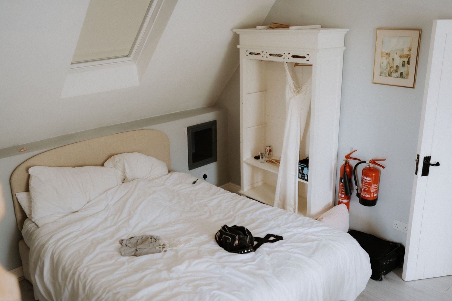 Minimalist white bedroom with unmade bed, wardrobe, and skylight in loft-style space with cream colored walls.
