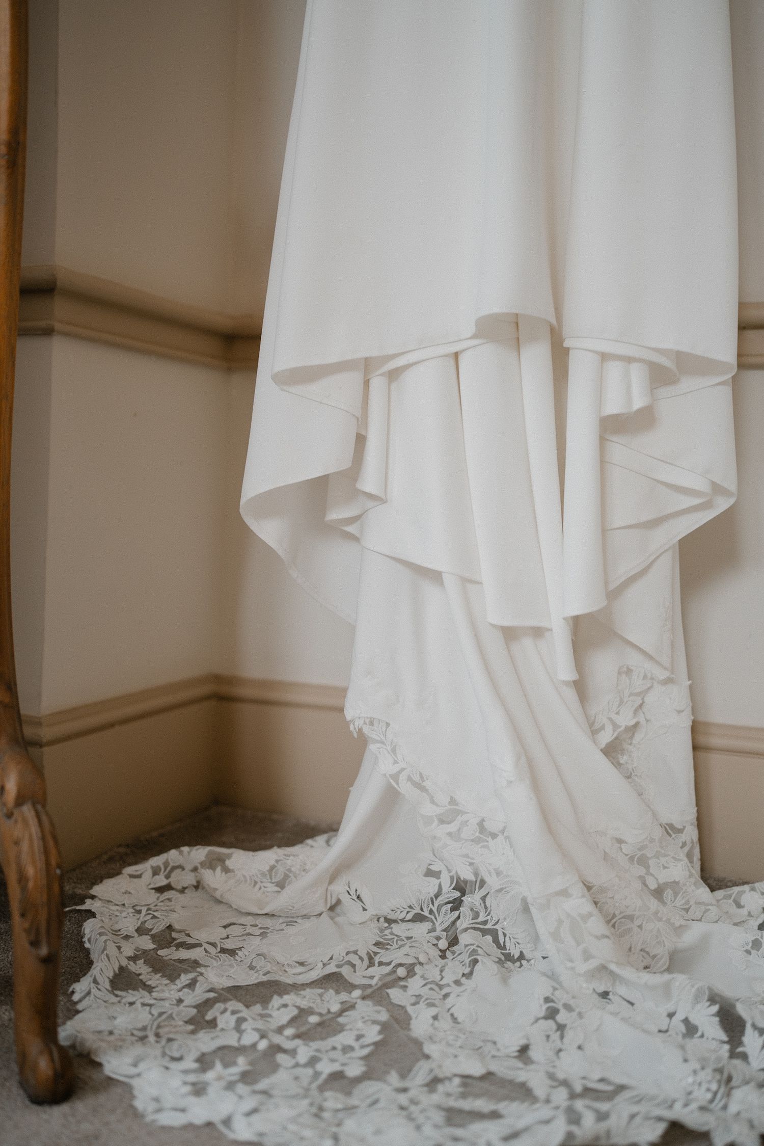 A flowing white wedding dress with delicate lace trim hangs elegantly, its train cascading onto the floor. Wedding at Nonsuch Mansion