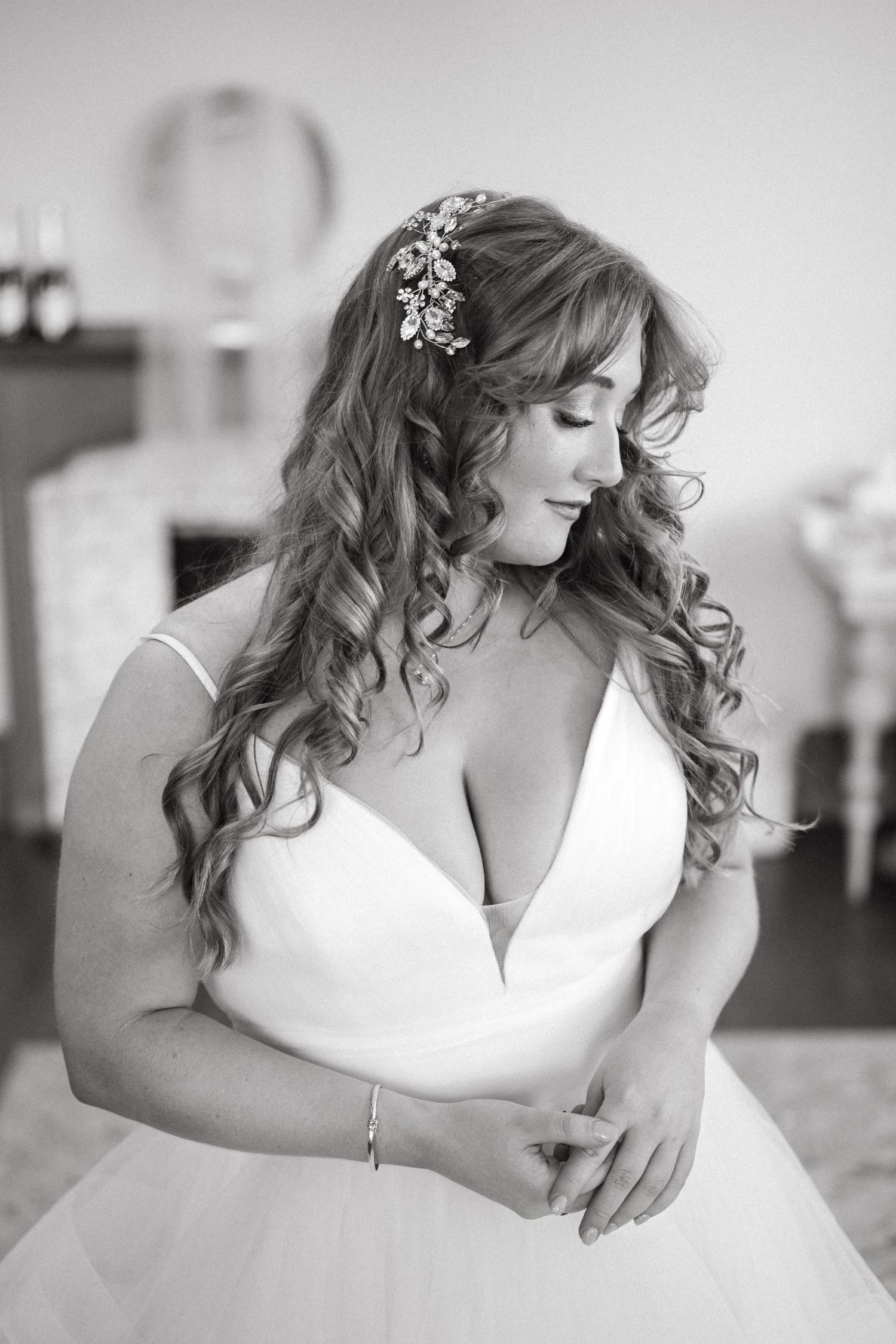 Elegant bride in white ball gown with curled hair and floral accessories poses in black and white.