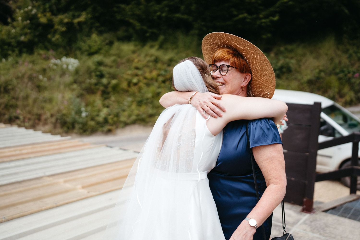 Two people sharing an emotional embrace on a wooden deck outdoors.