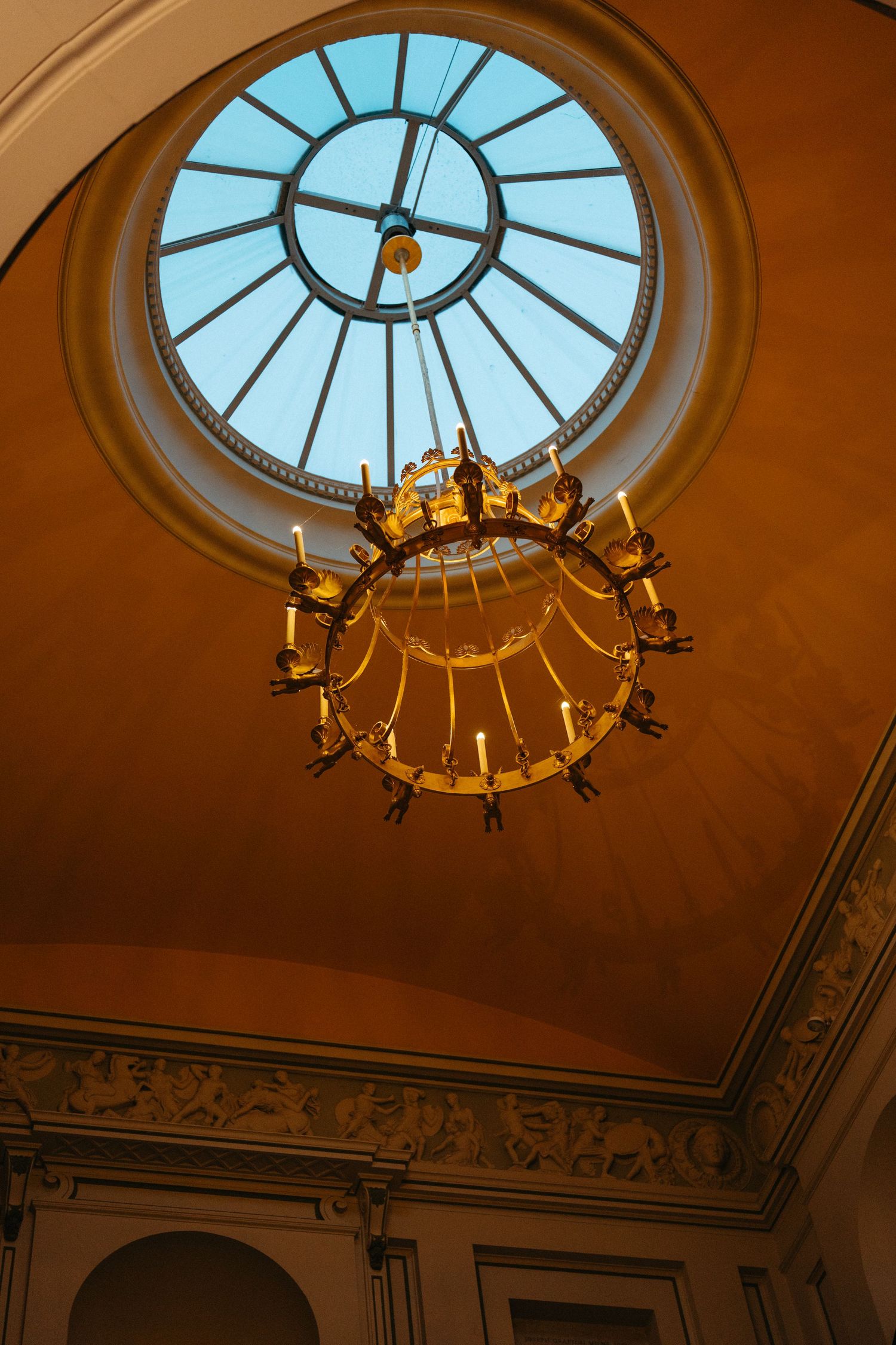 Elegant circular skylight and chandelier in a historic building's domed ceiling.
