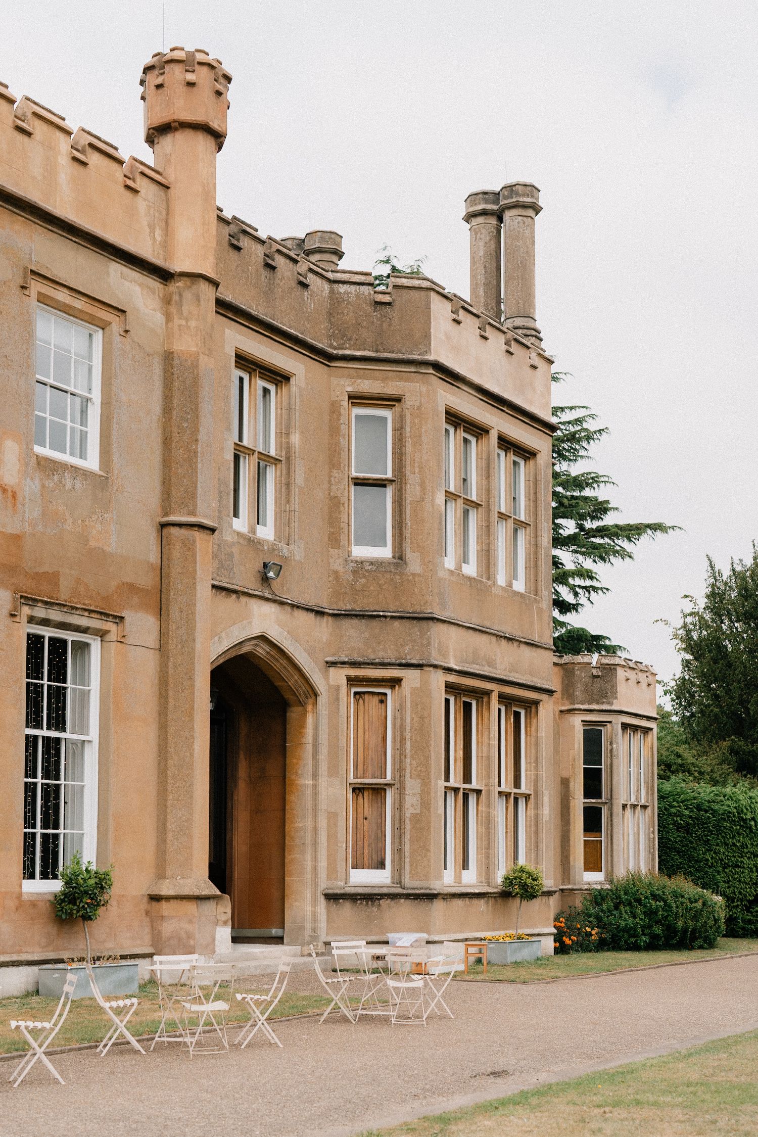 Elegant historic stone manor house with Gothic architectural details and outdoor seating on a paved terrace.