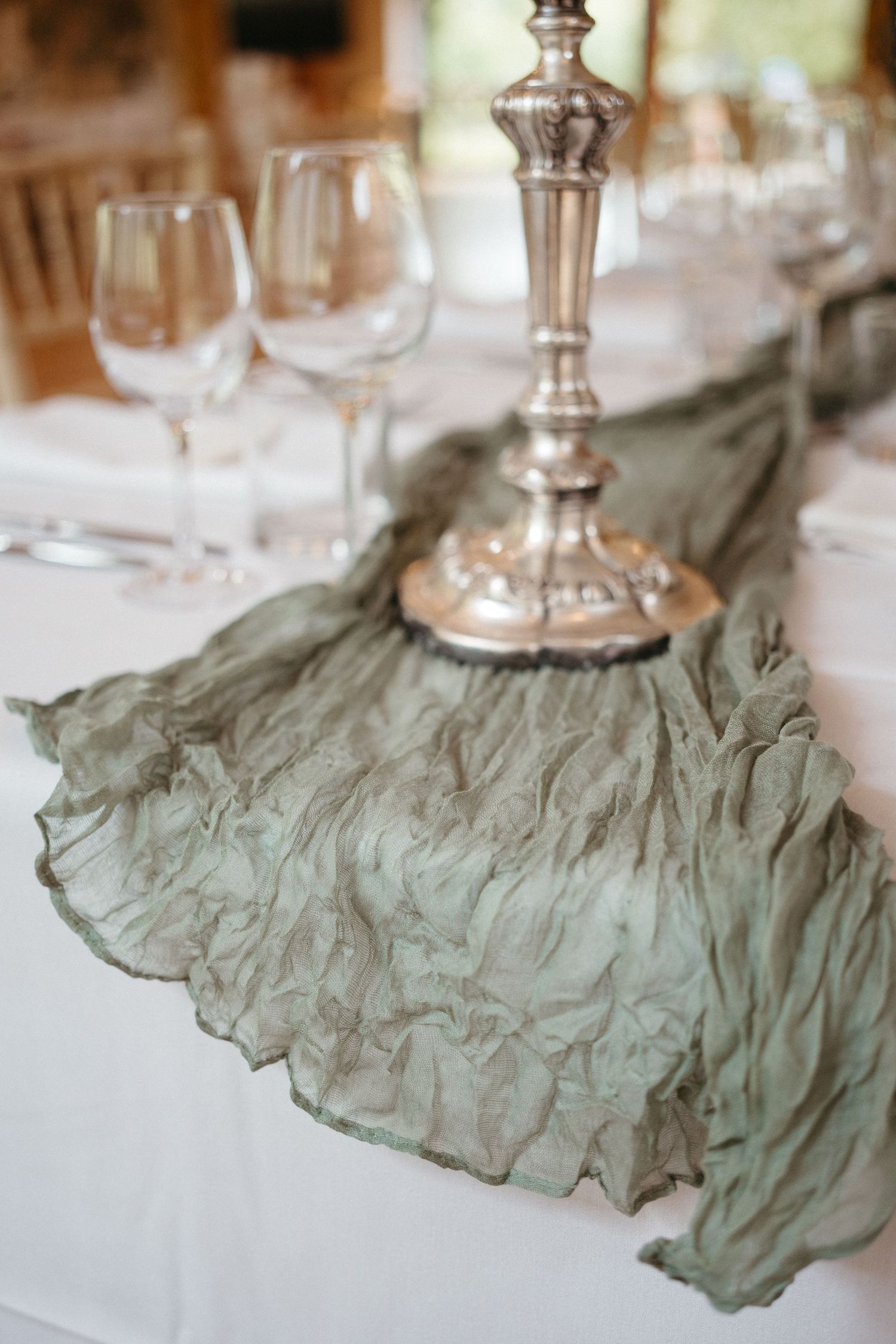 Elegant table setting with silver candlestick and sage green ruffled runner on white tablecloth.
