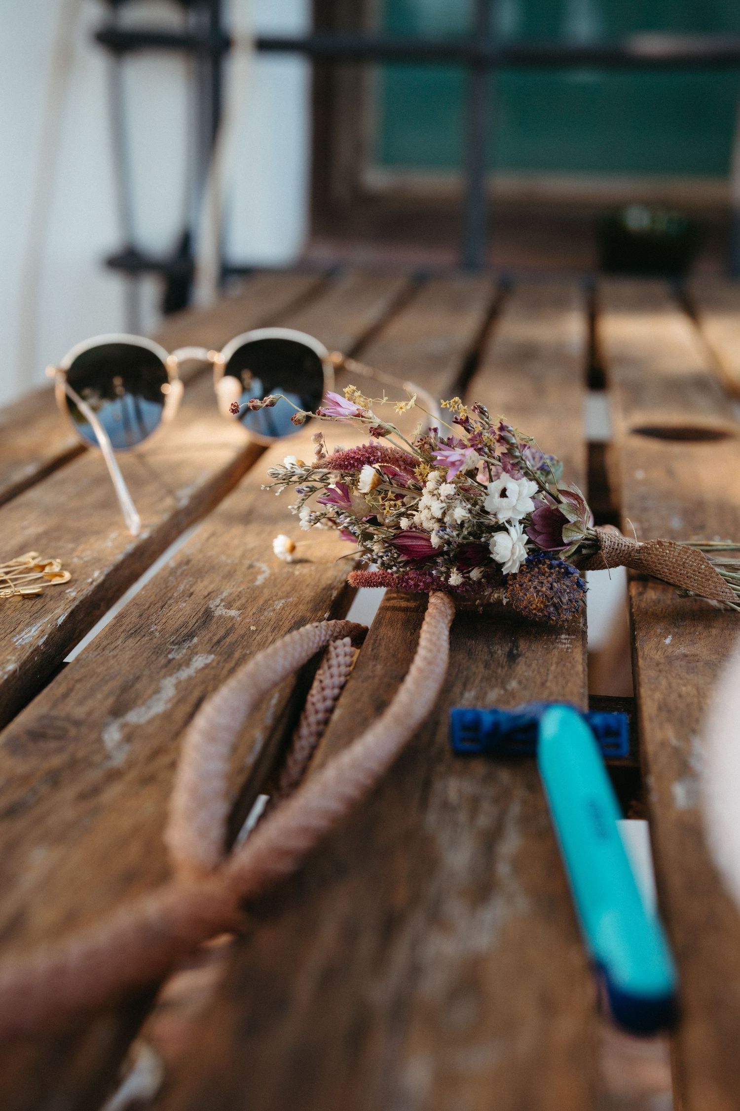 Two hands display a delicate floral crown with dried flowers laid on a rustic wooden table.