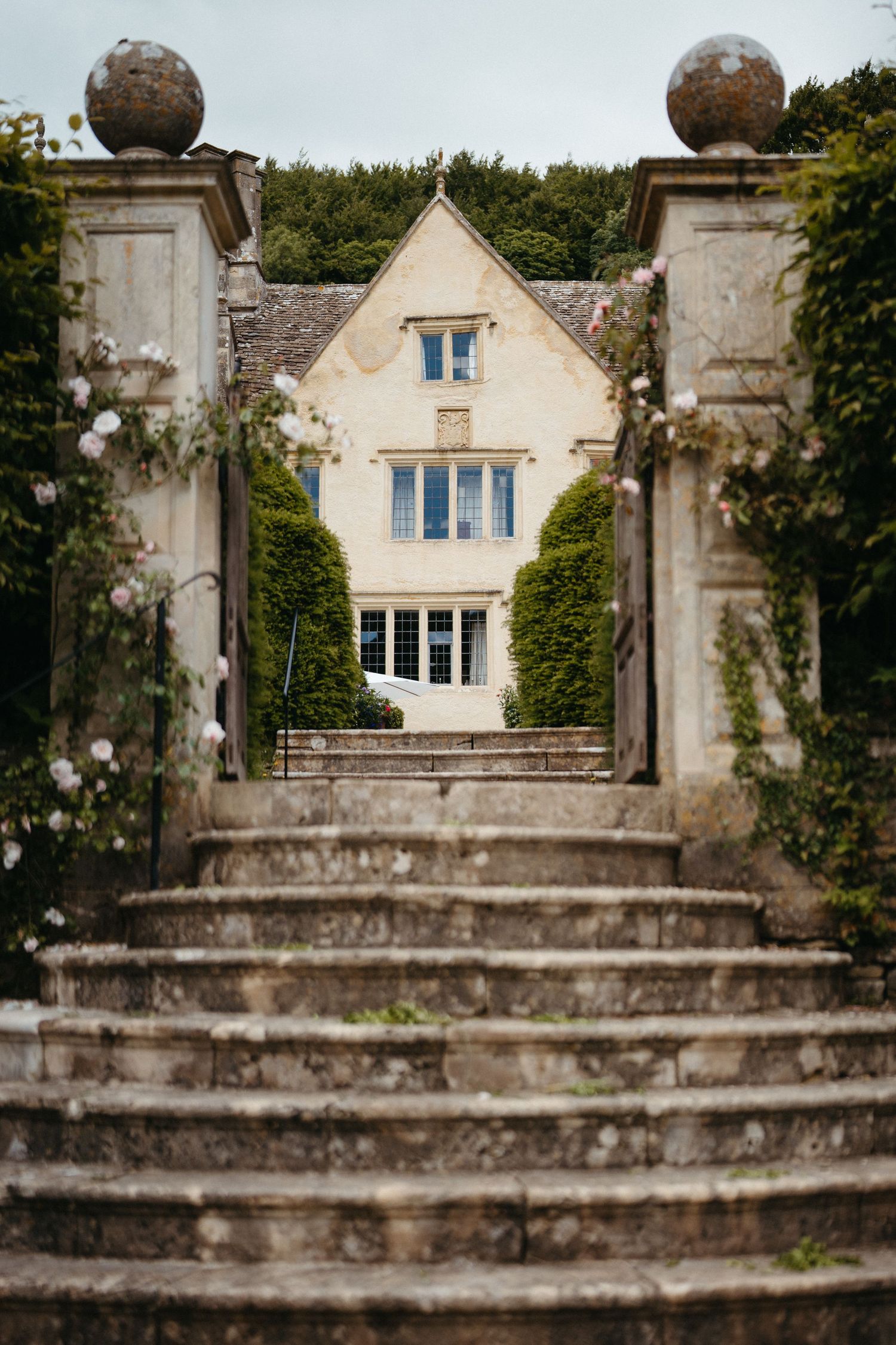 Grand stone mansion viewed through pillared entrance with stone steps leading to elegant facade.
