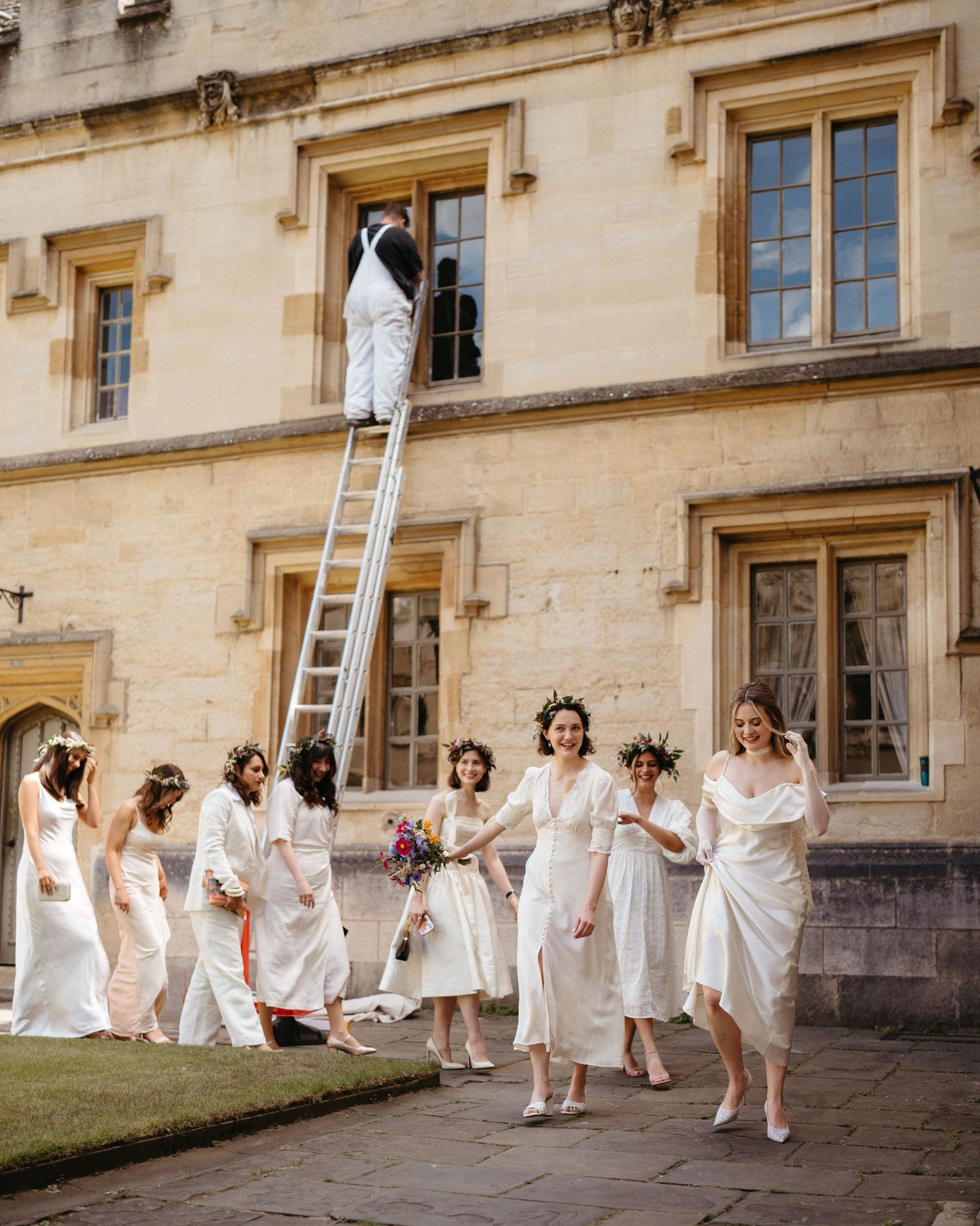 A sequence of dancing figures in white dresses spread along the exterior wall of a historic stone building.