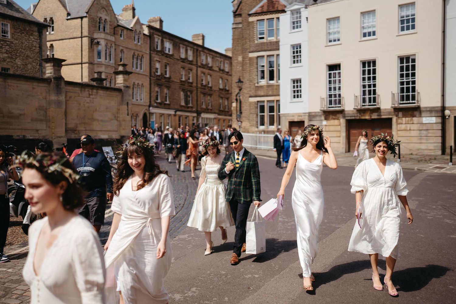 A group of people in white clothing walk down a historic cobblestone street between old stone buildings in Edinburgh.