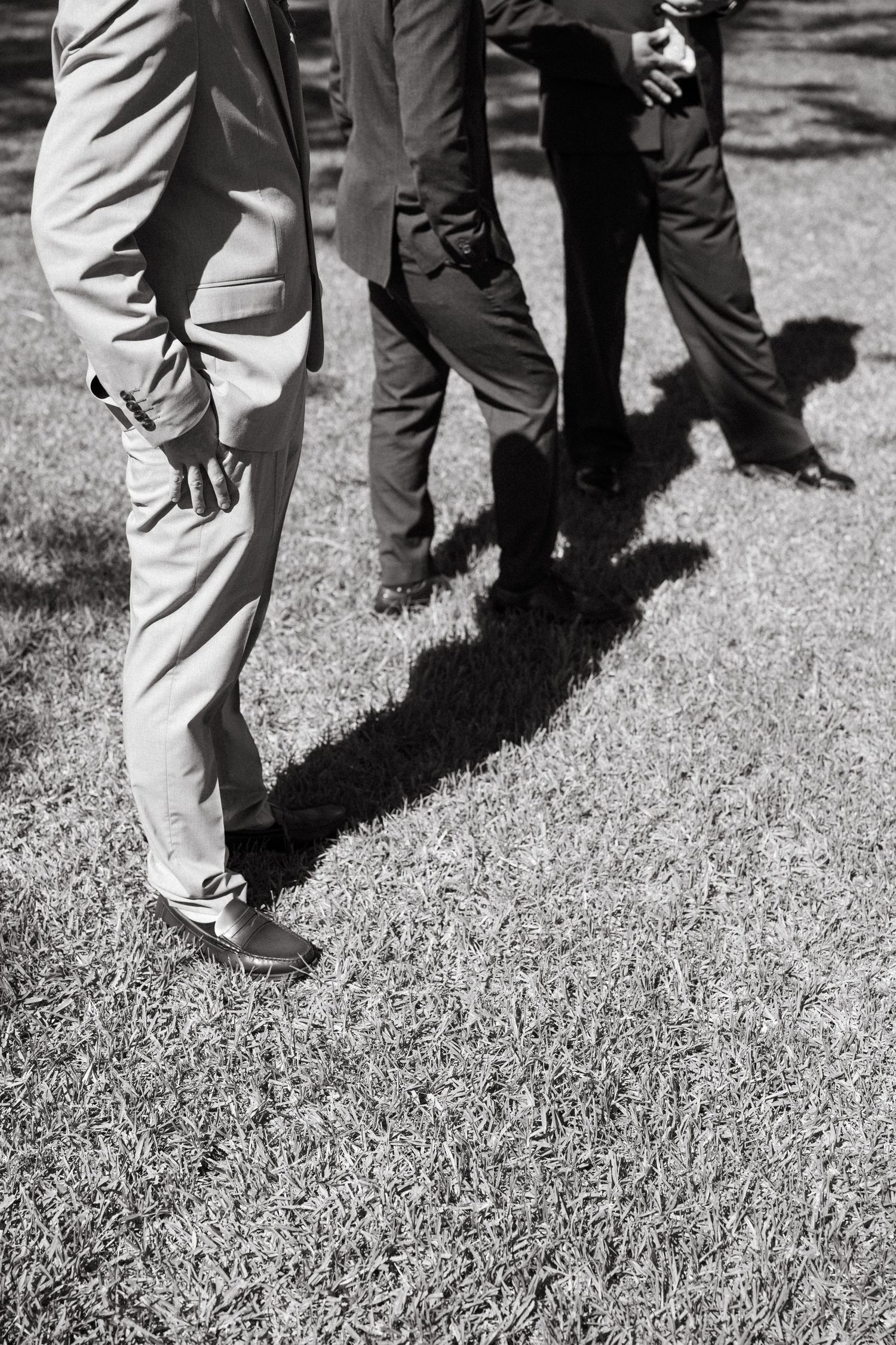 Black and white photo showing legs wearing khaki pants standing on grass with dramatic shadows cast on the ground.