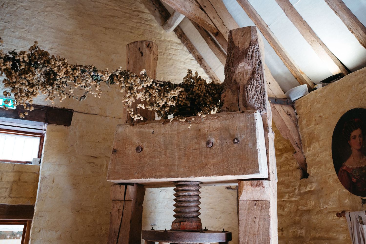 Rustic white stone interior with exposed wooden beams and a decorative garland in a historic barn setting.