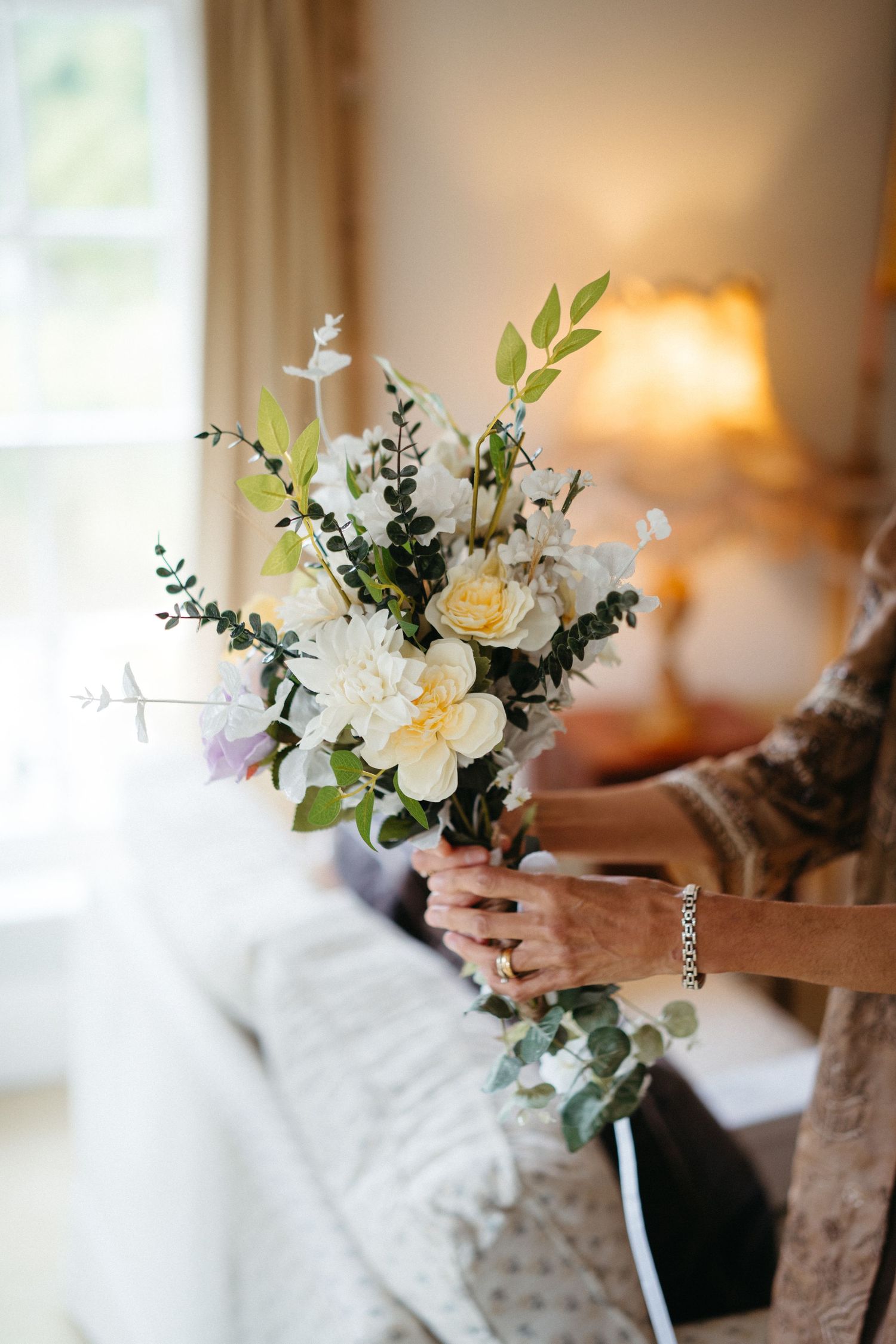 A delicate white and green wedding bouquet with roses and eucalyptus held against a soft background.