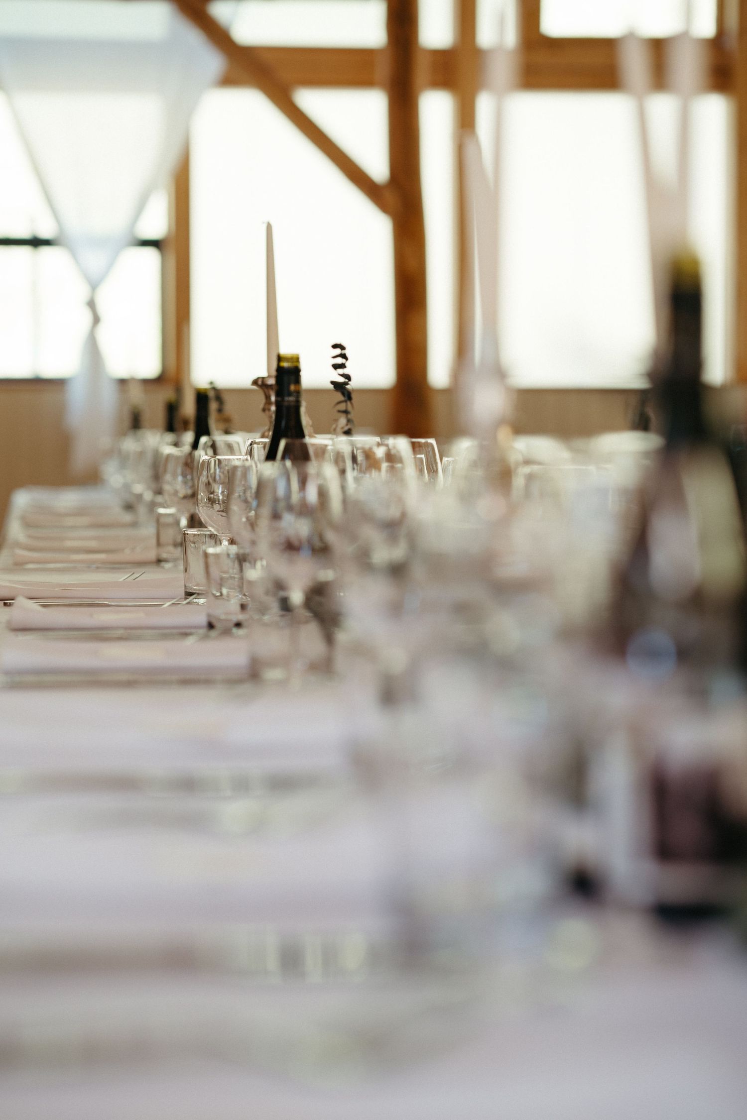 Elegant table settings with glassware and white linens in a sunlit banquet hall create an upscale dining atmosphere.