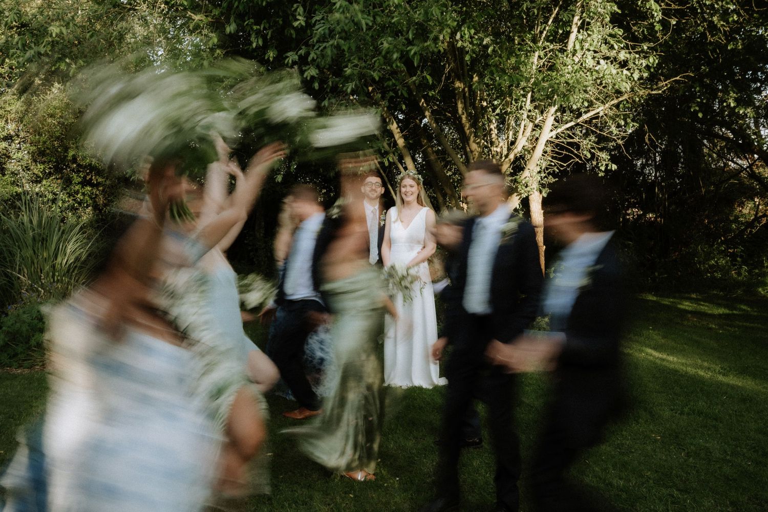 Artistic motion blur photograph of a wedding party dancing and celebrating in a lush garden setting.