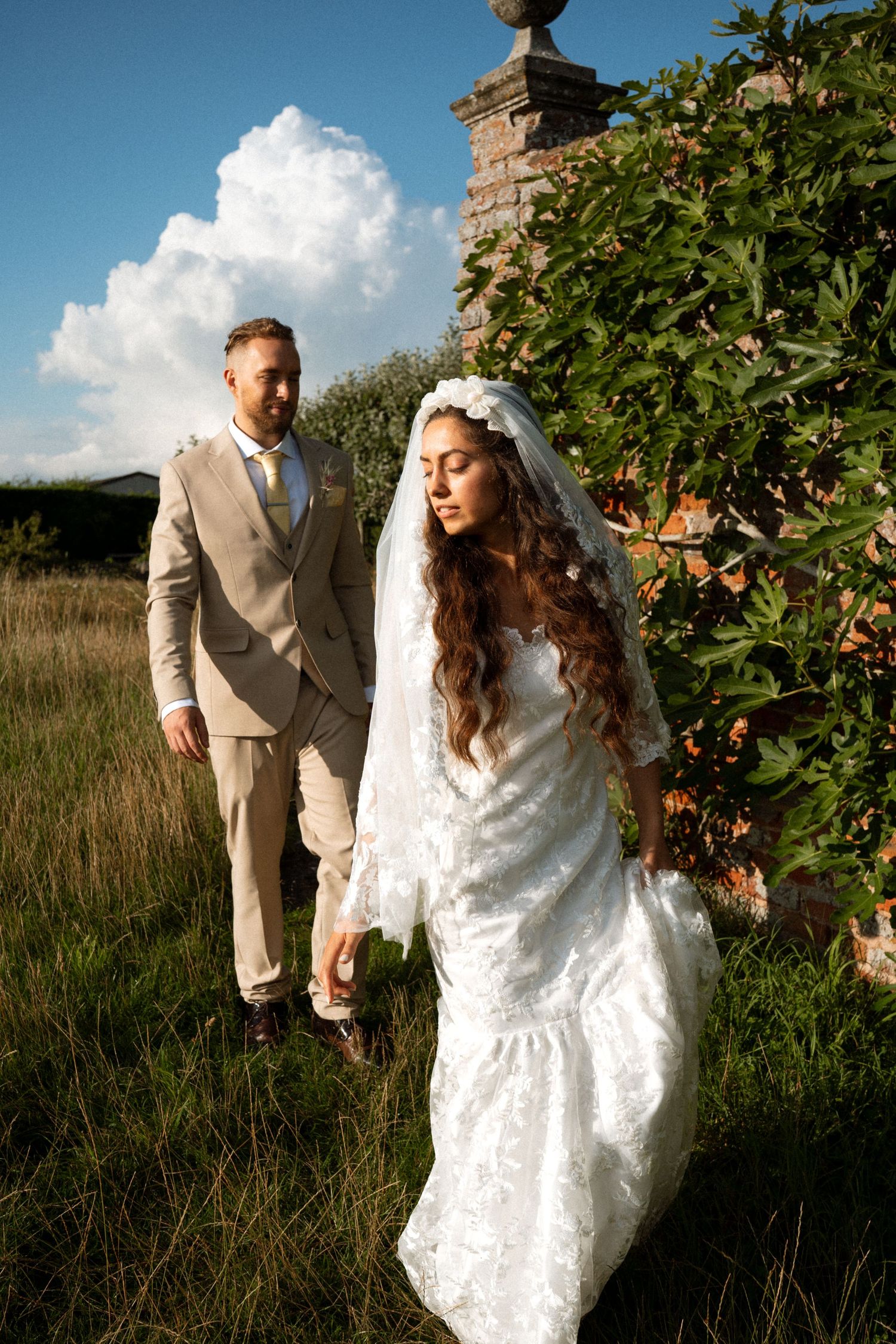 A couple enjoys their wedding day outdoors among tall grass and greenery in a rustic countryside setting.