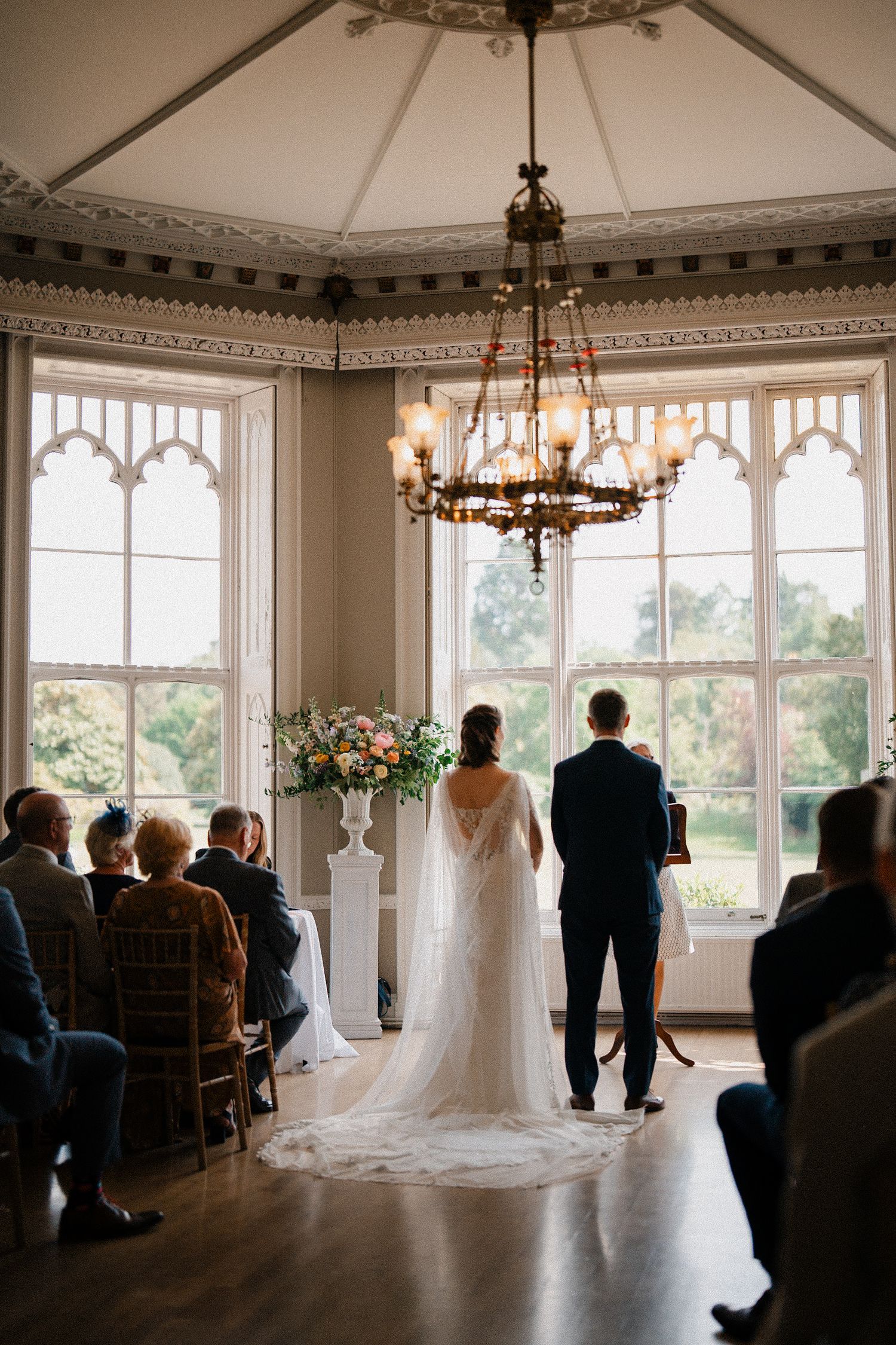 Elegant wedding ceremony in a Victorian room with ornate chandelier and Gothic windows. Wedding at Nonsuch Mansion